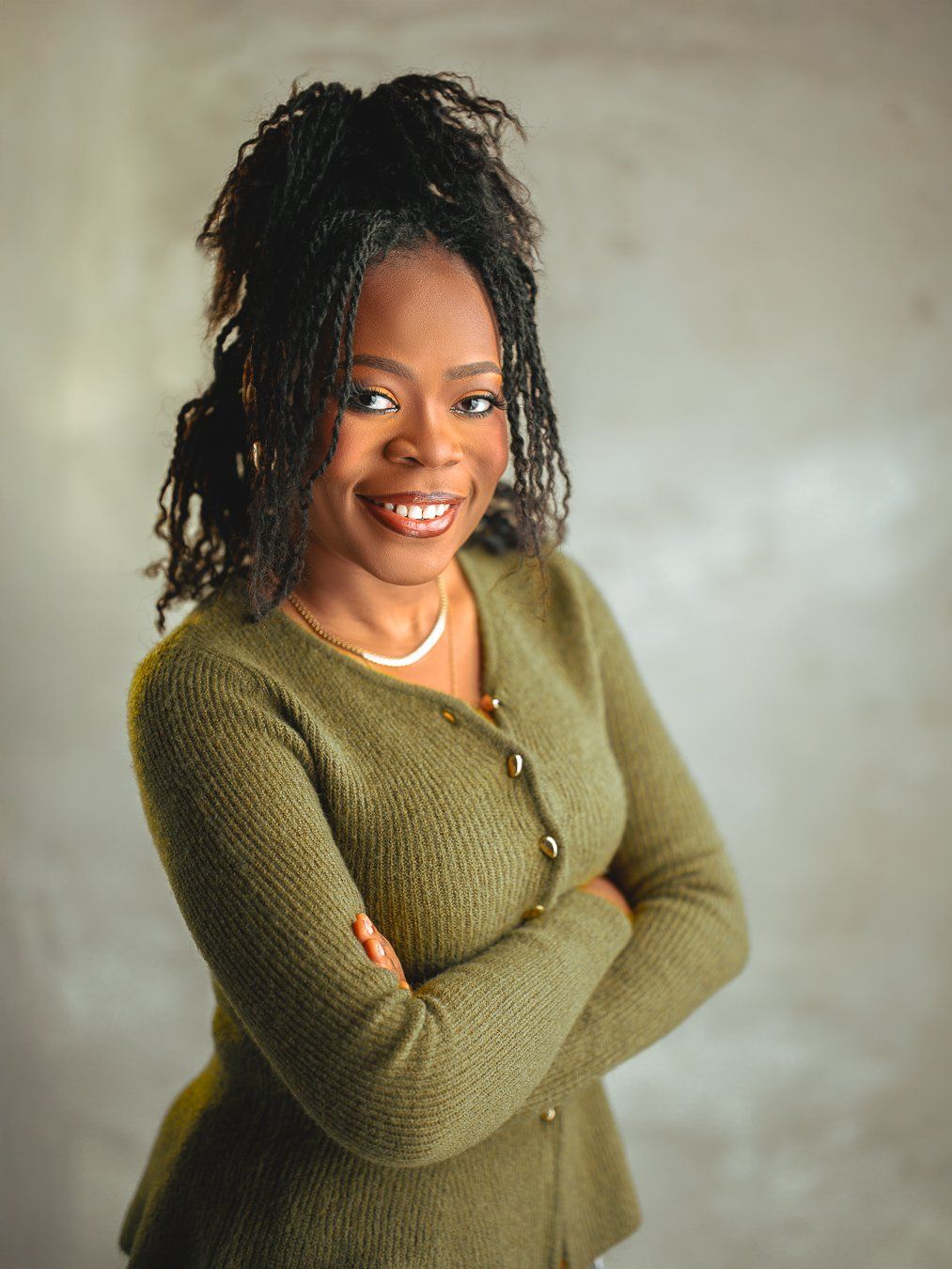 Smiling lady wearing a green knit sweater with braided hair styled upward poses against neutral background.
