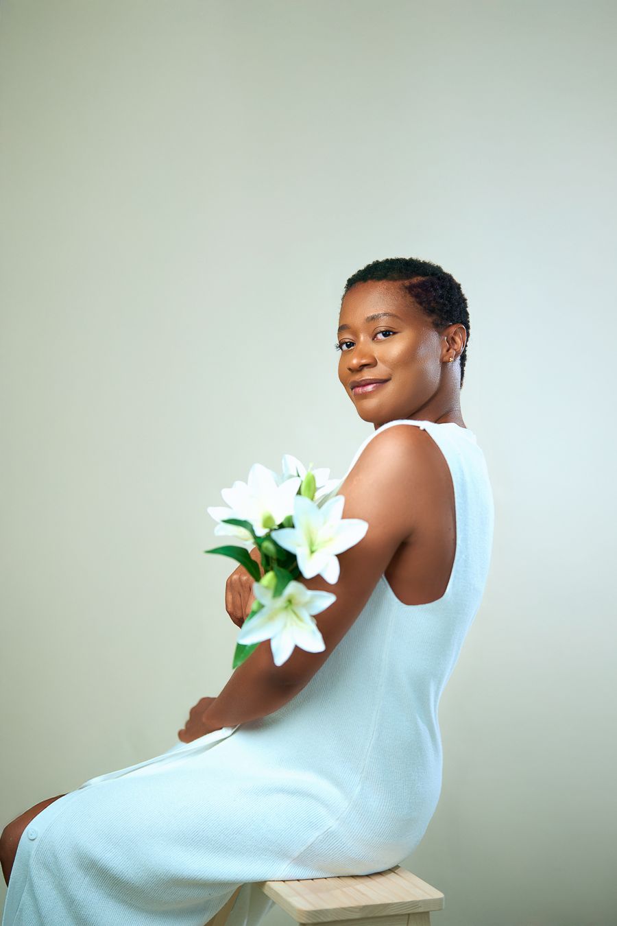 An artistic portraits featuring a lady in white against a pale background with a white lily flower.