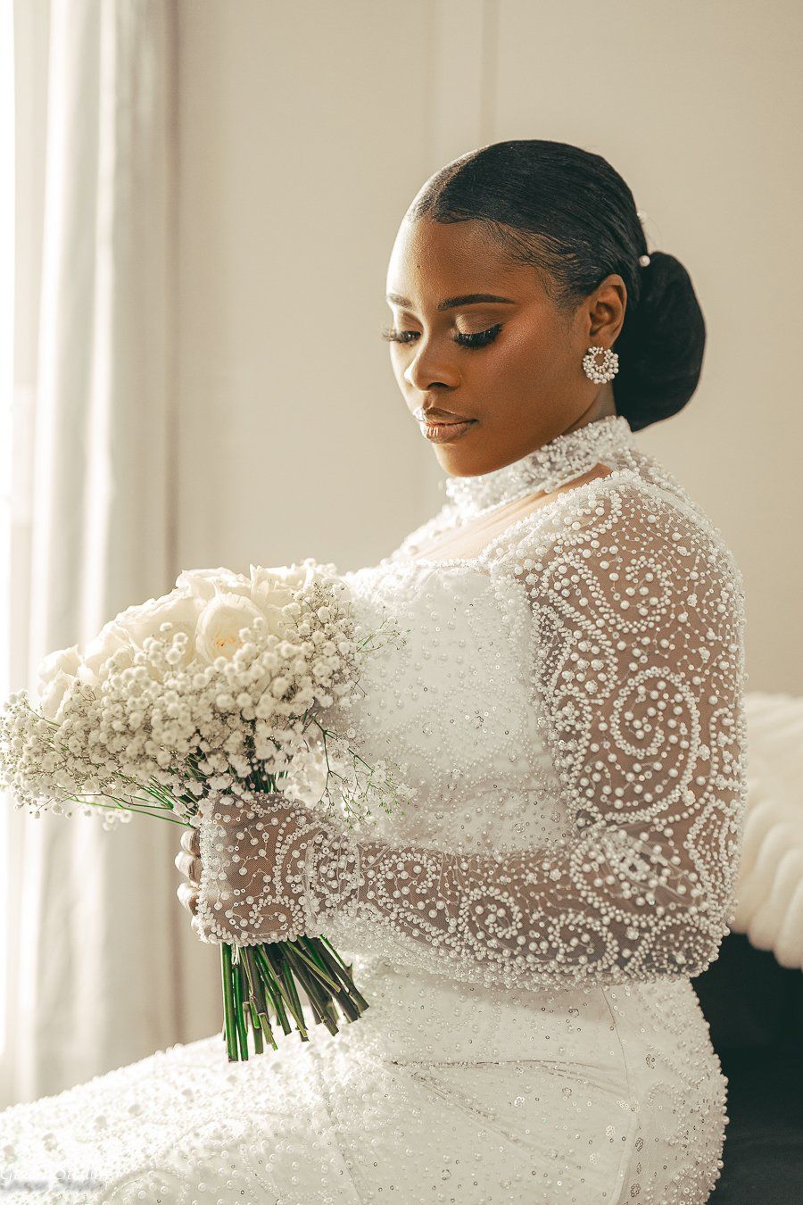 Elegant bride in a long-sleeved white beaded wedding gown with intricate pearl details poses with a bouquet.