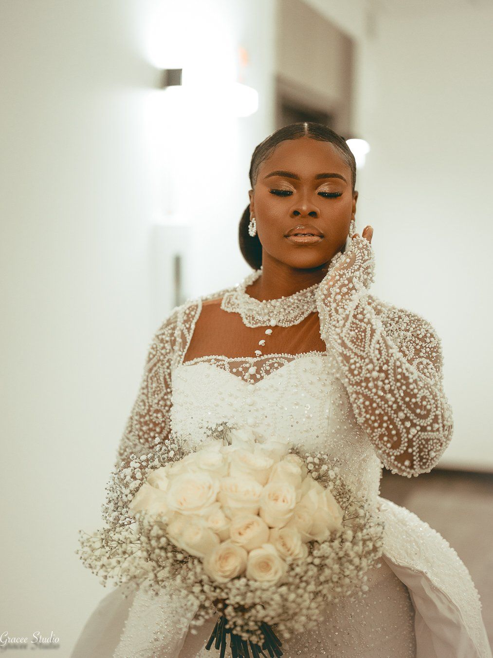 Elegant bride in long-sleeved beaded lace gown and white floral bouquet