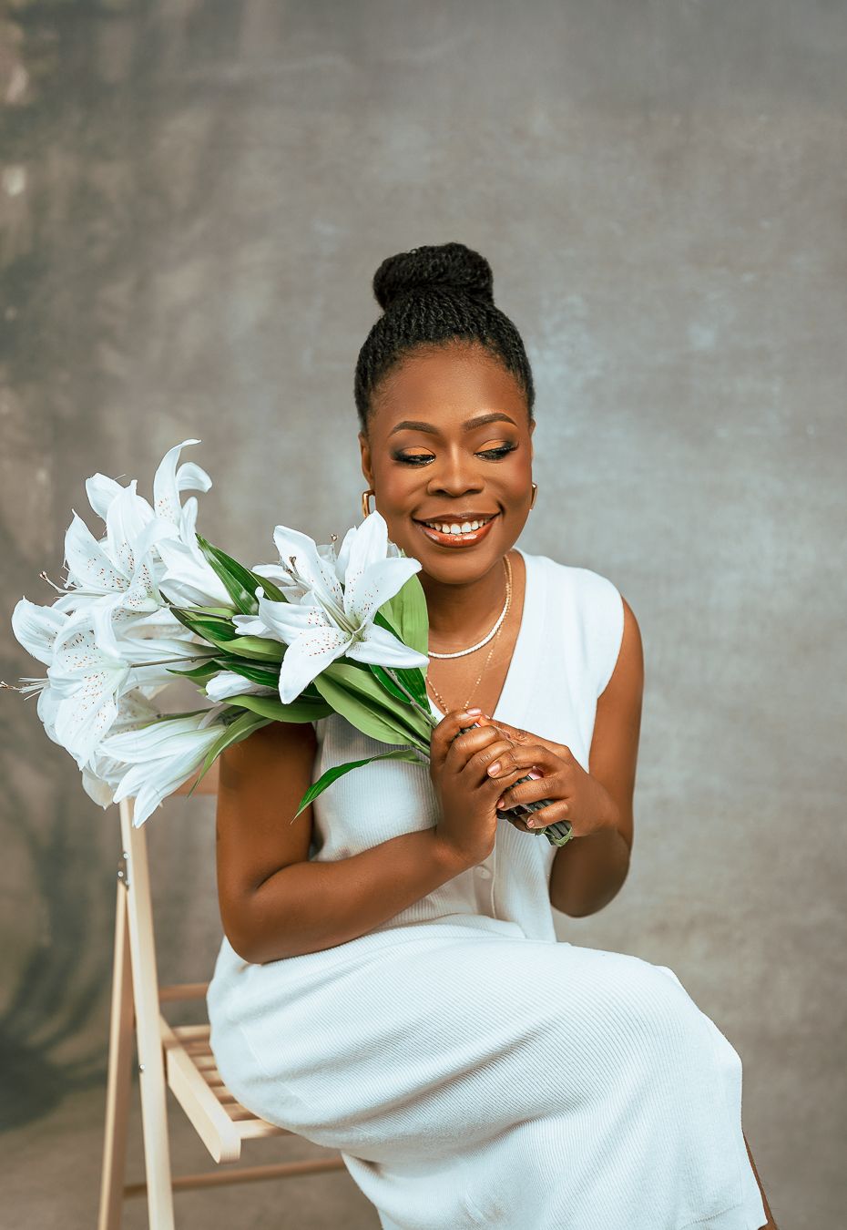 Portrait of a young lady holding white lilies and a white dress against a textured grey backdrop.