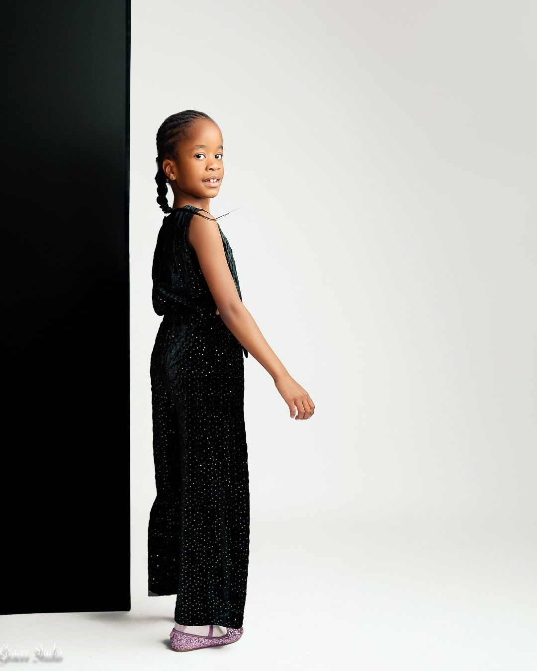 A kid in a black dress poses against a white backdrop in the studio