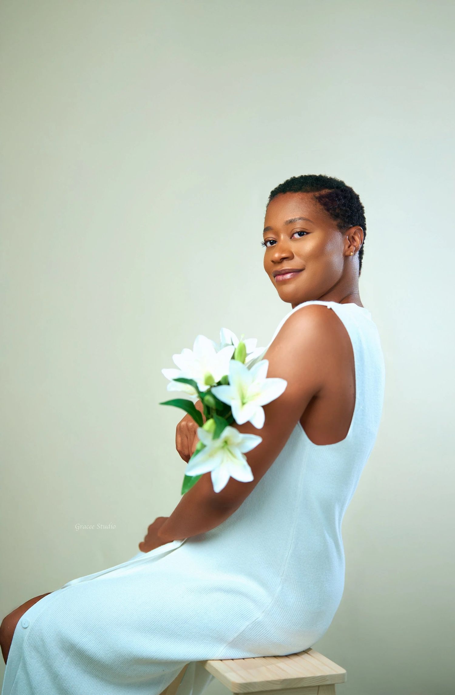 An artistic portraits featuring a lady in white against a pale background with a white lily flower.