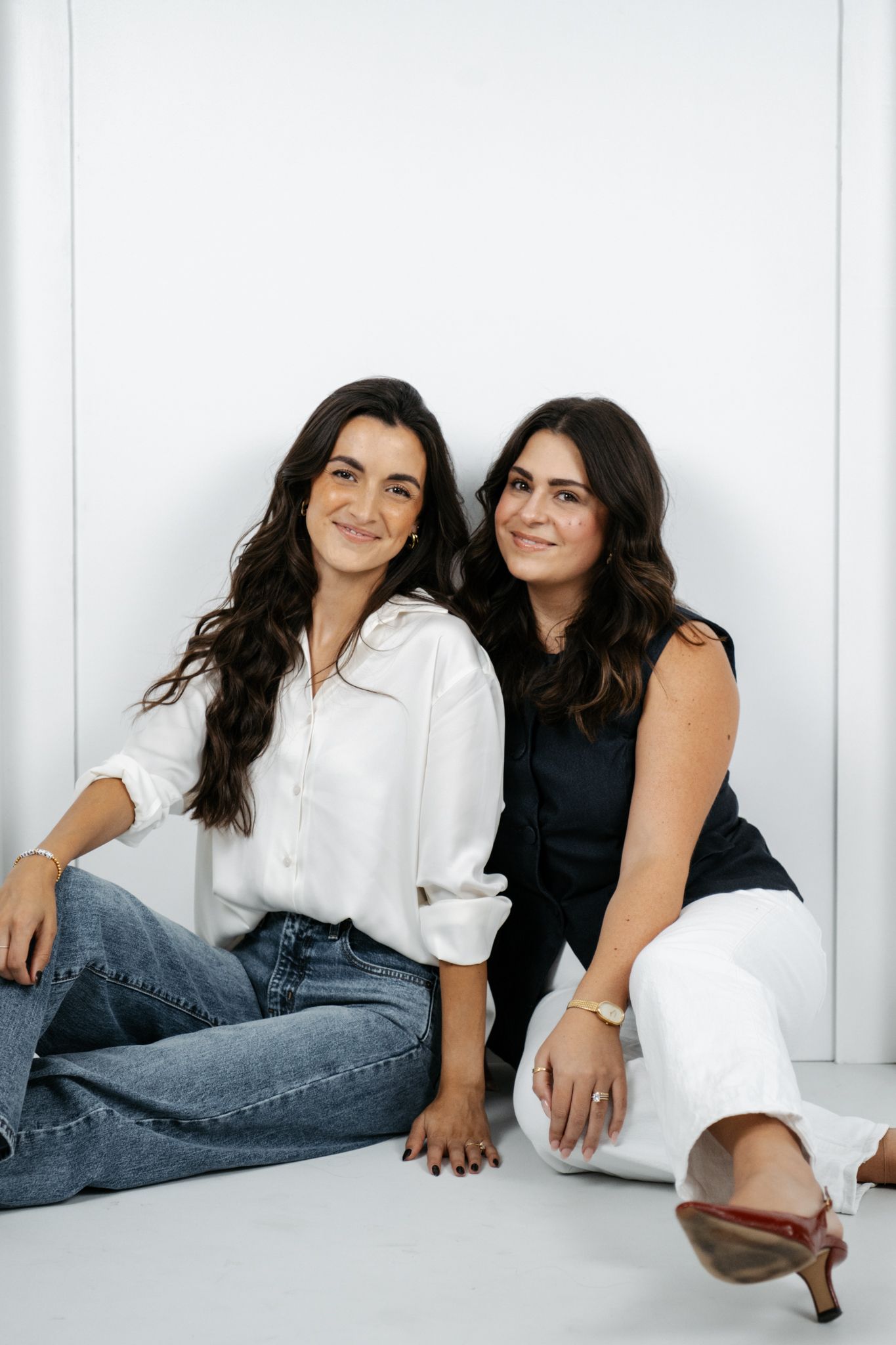 Two women in contrasting black and white outfits posing playfully on the floor during a studio photoshoot.