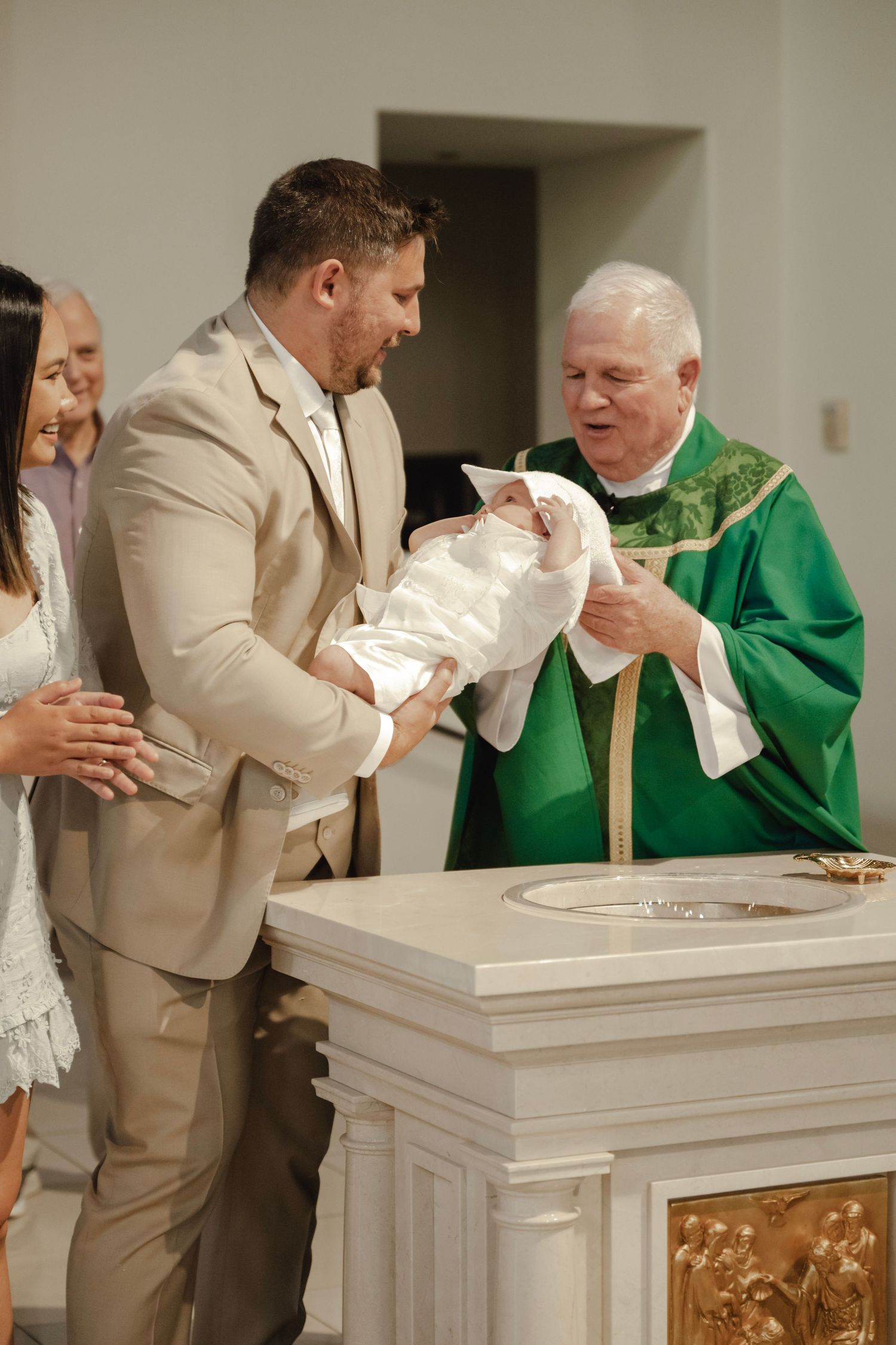 Religious baptism ceremony taking place at church altar with priest in green robes.