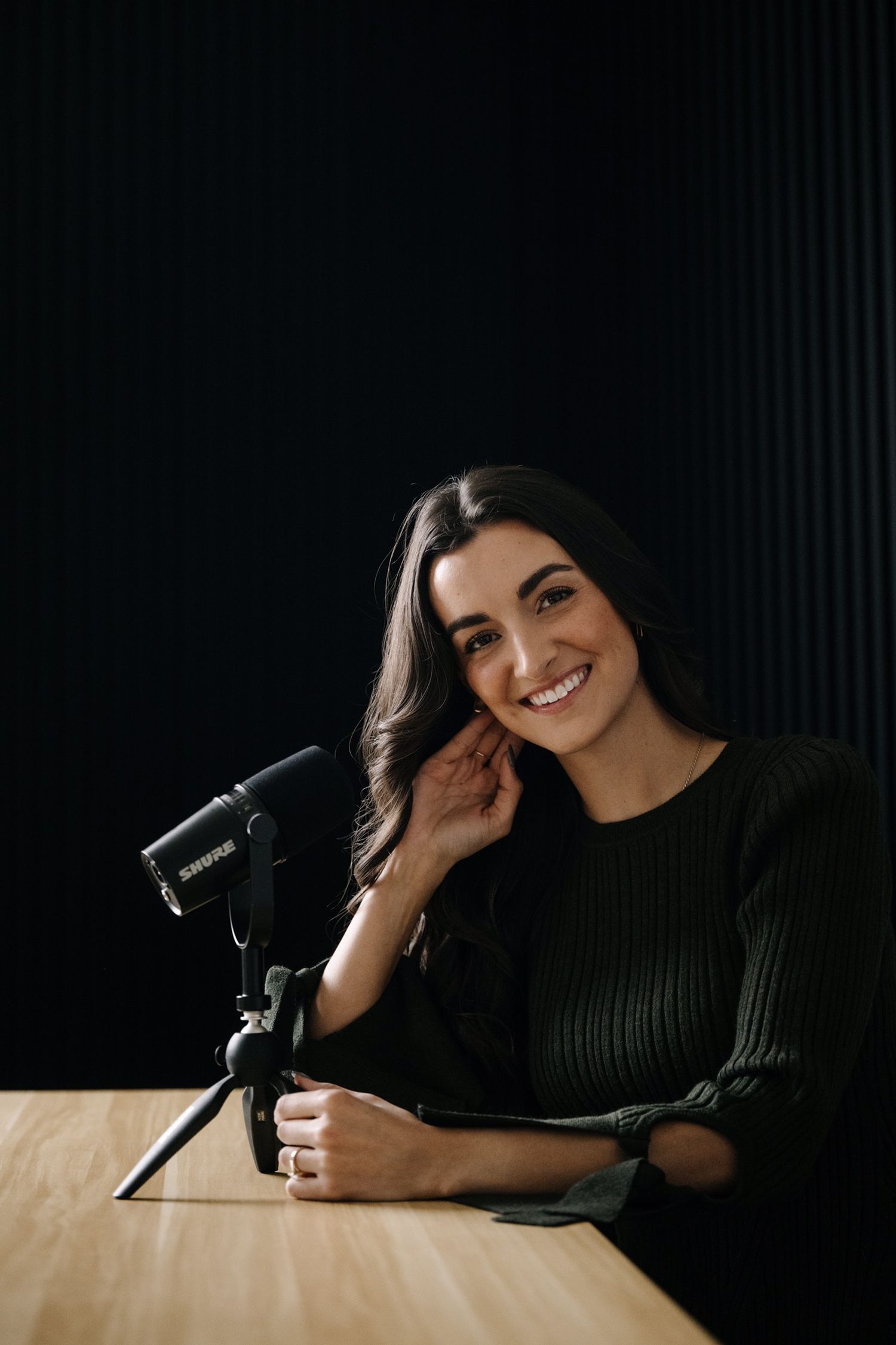 Studio portraits with dark background showing person with microphone in black sweater.
