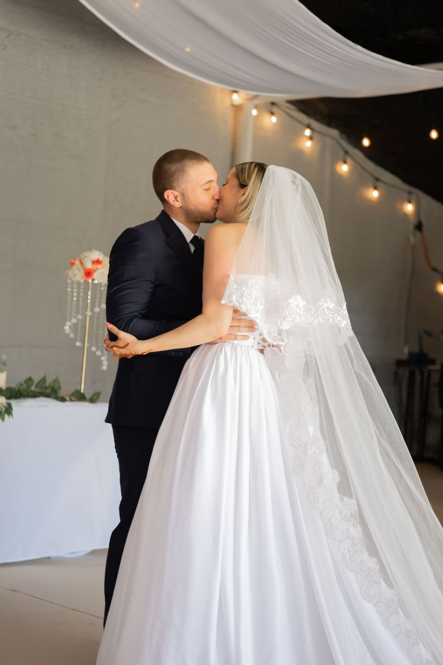 Wedding couple in elegant attire sharing intimate moments under string lights.