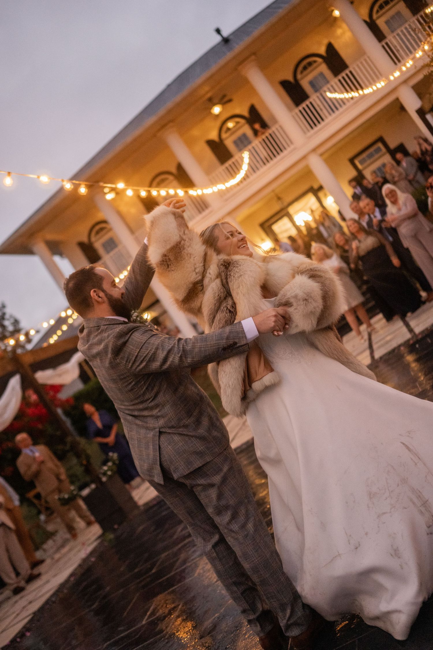 A couple performs a dramatic dance dip during a wedding reception under twinkling lights and white columns.