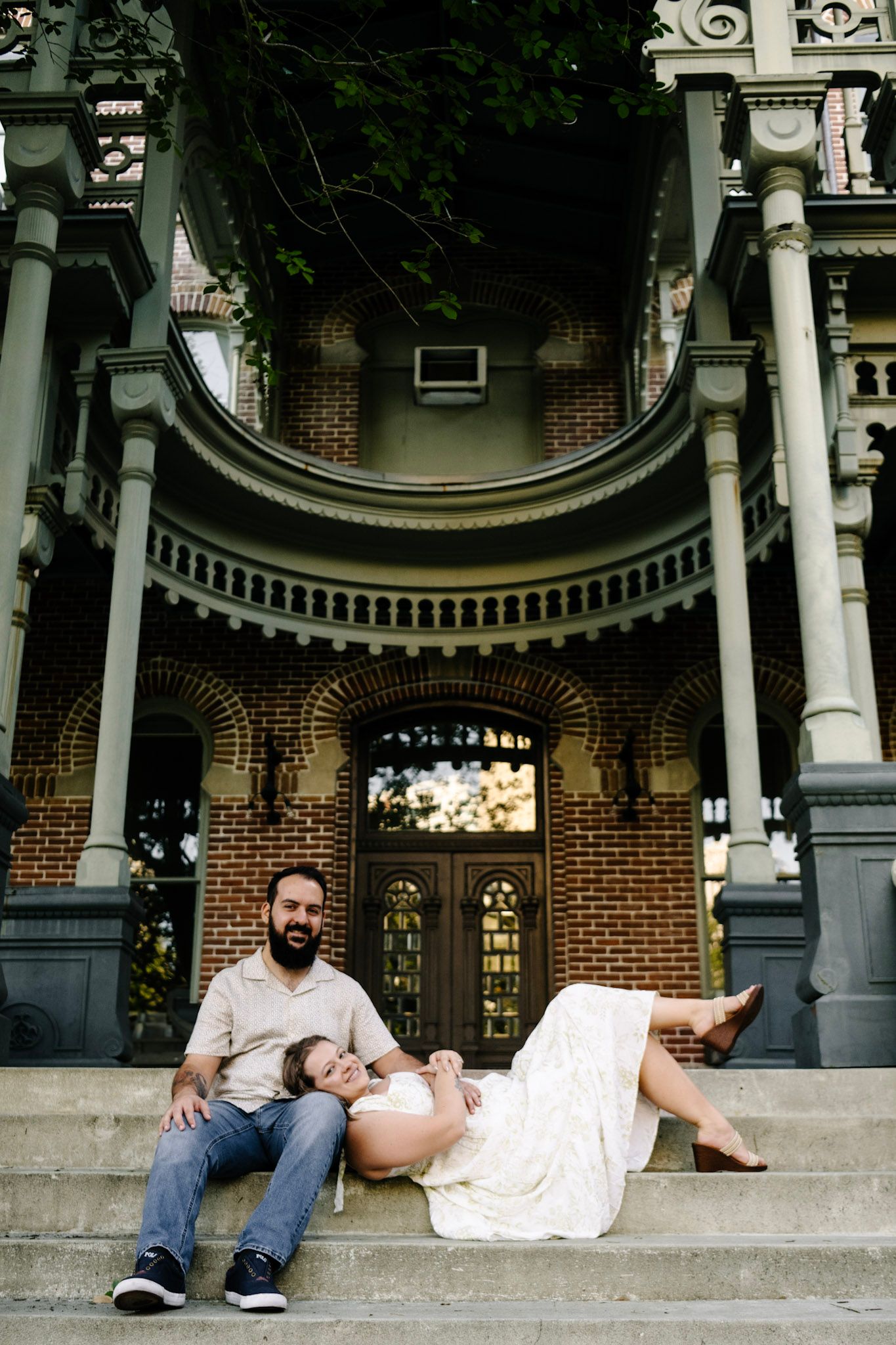 A couple relaxing on ornate stone steps of a historic brick building with architectural details.