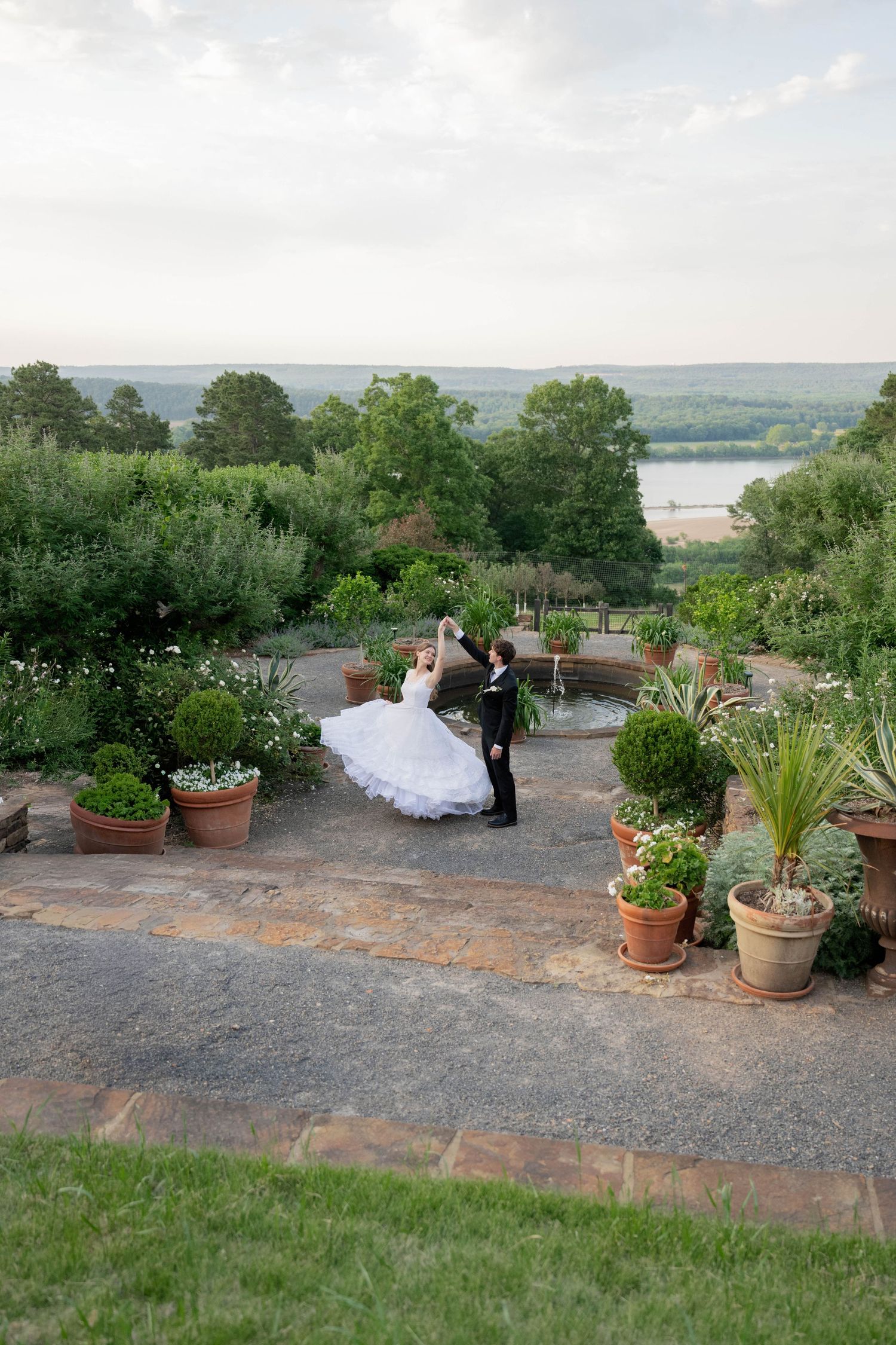 Bride and groom dancing in a lush garden terrace with scenic river views in the background.