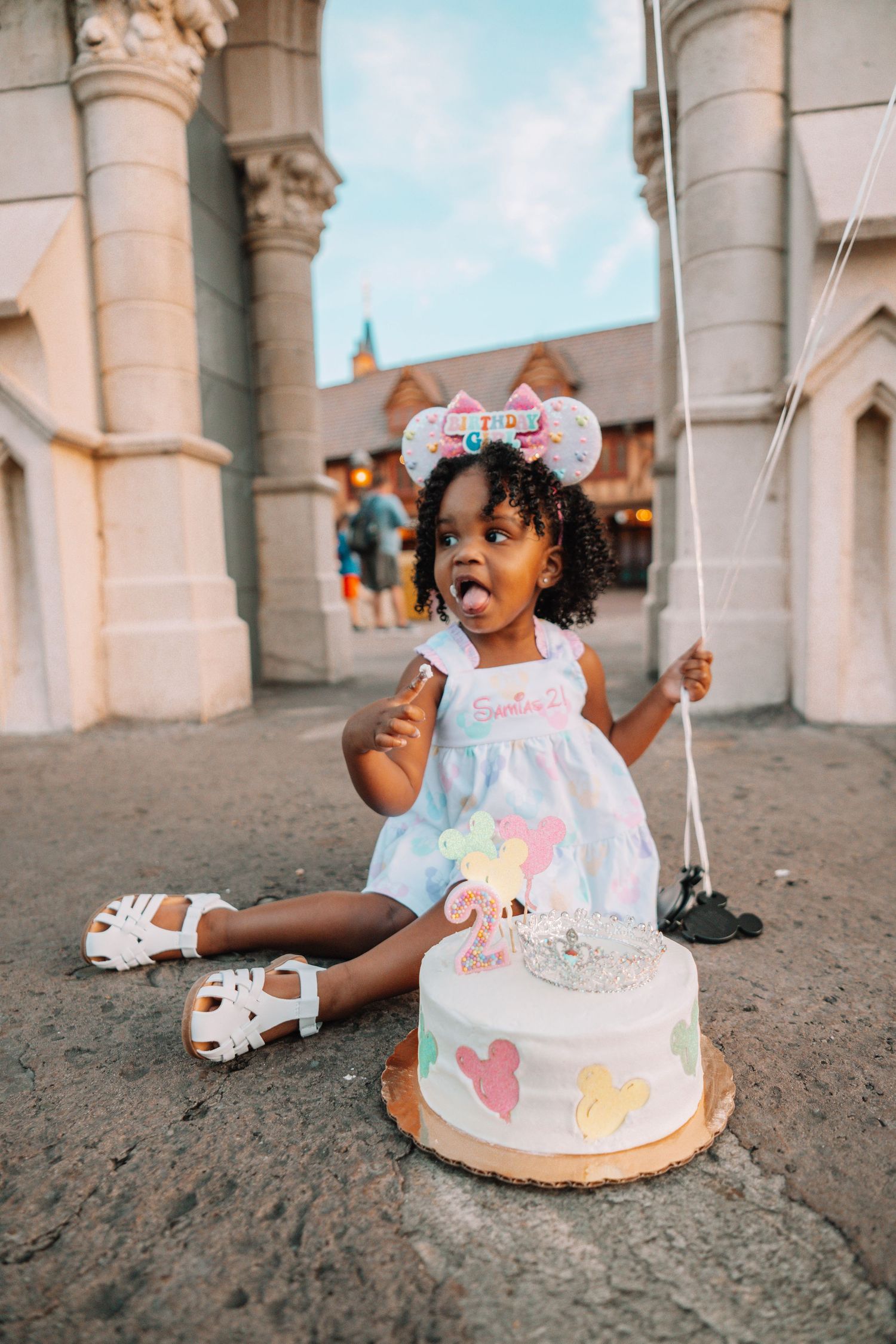 Birthday celebration with cake and Mickey ears in front of a castle.