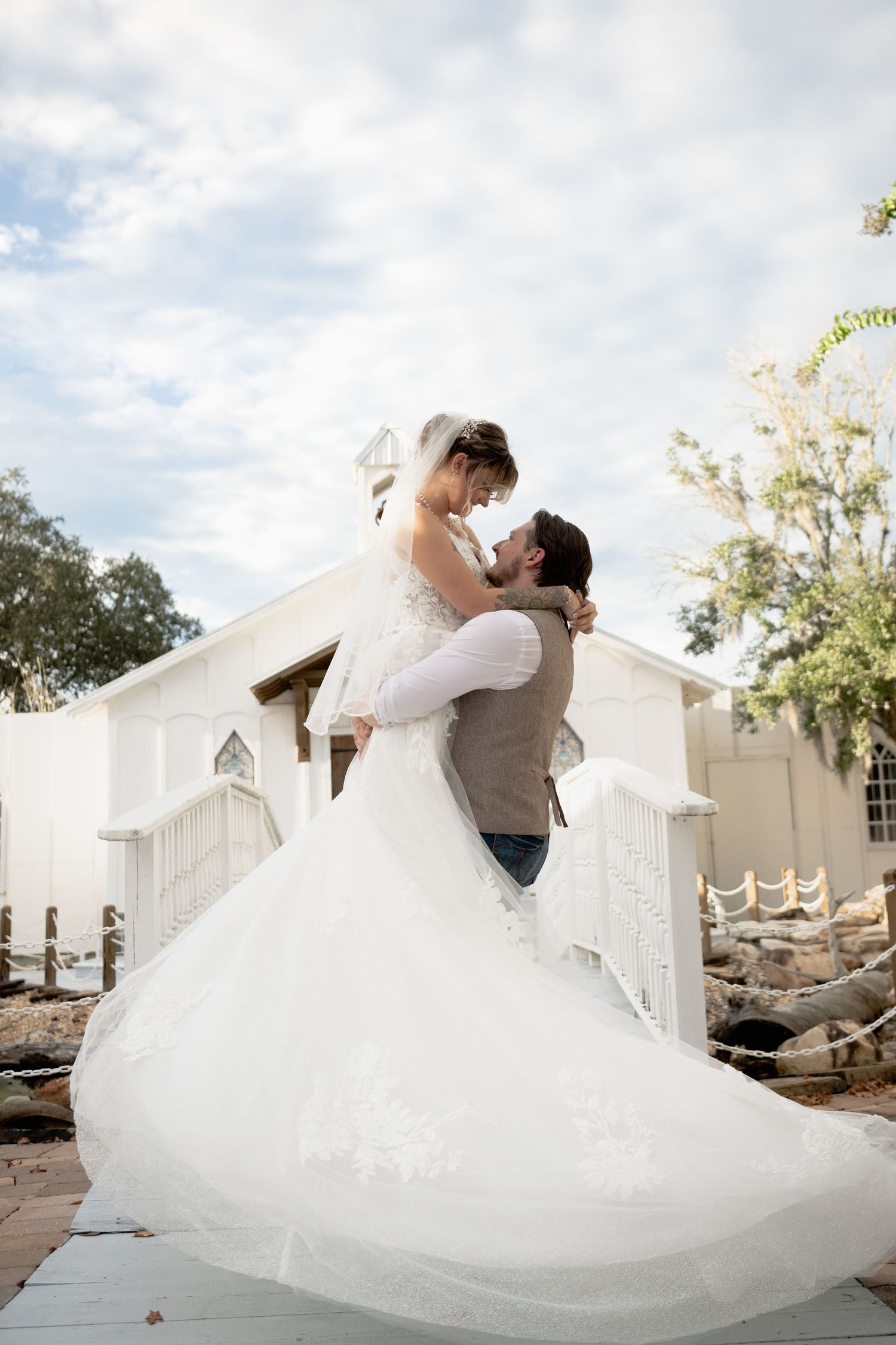 Wedding couple in white dress and grey suit dancing and dipping dramatically against a cloudy sky.