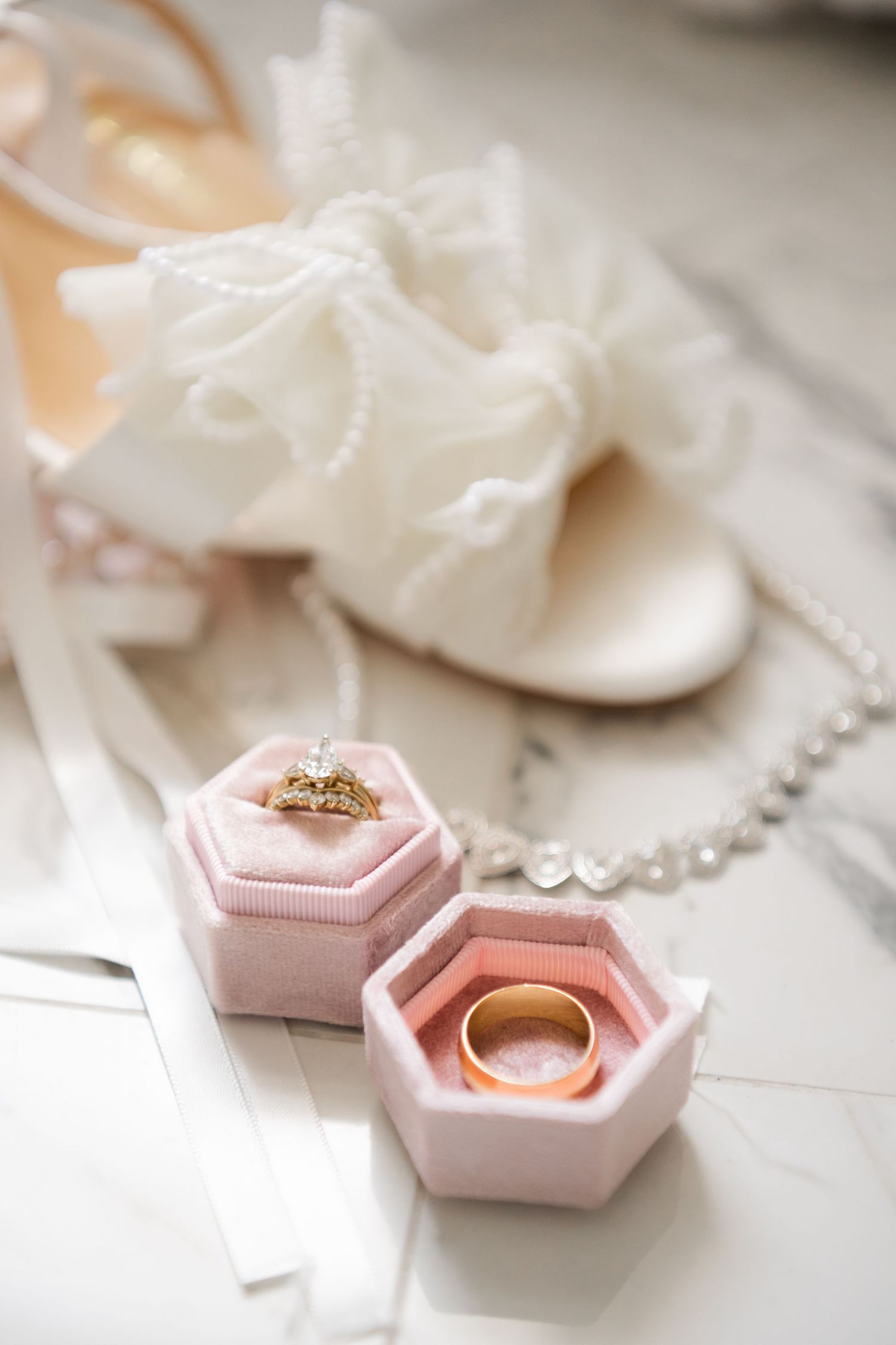 Delicate wedding details with pink hexagonal ring boxes and pearl jewelry on white background.