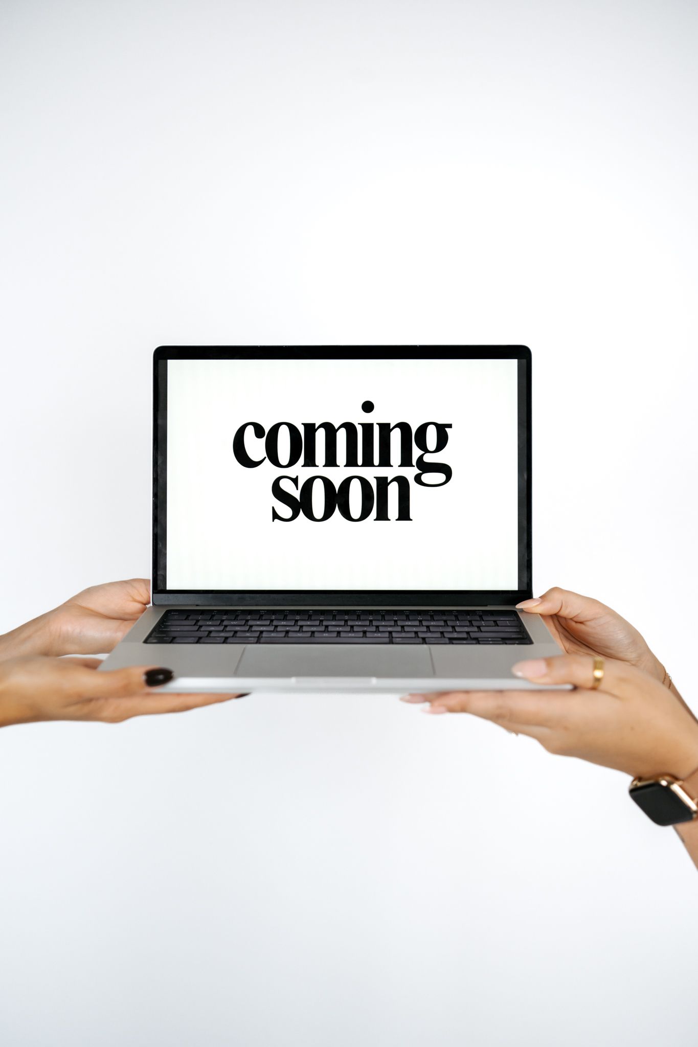 Hands holding laptop displaying 'Coming Soon' text on white background.
