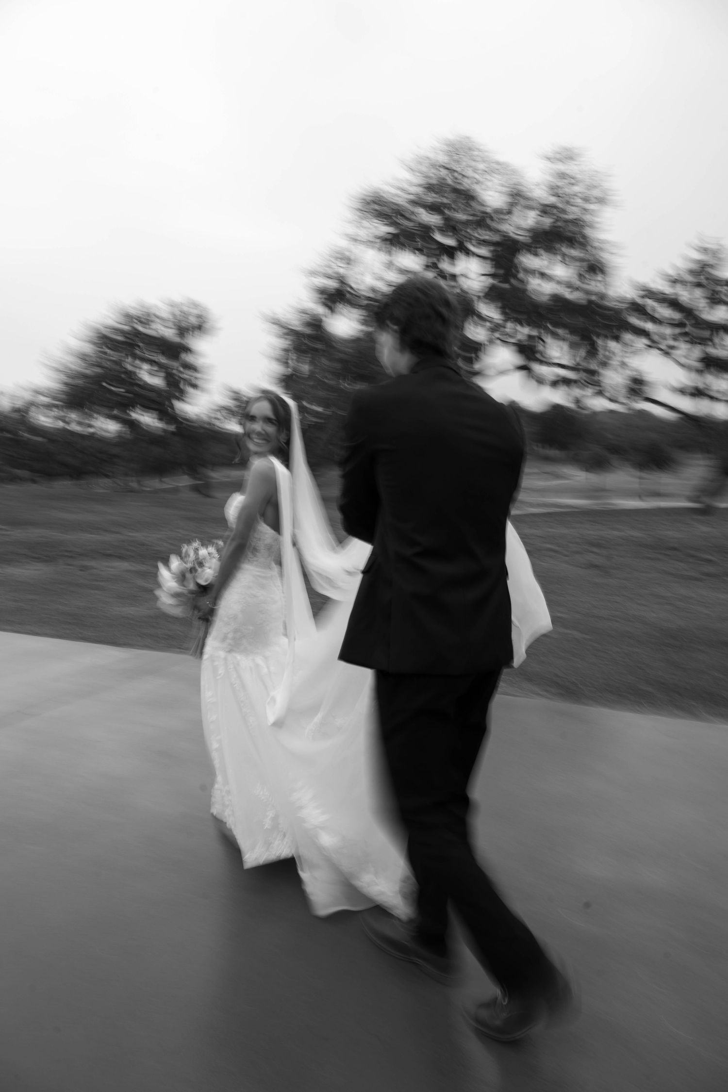 Black and white photo of a bride and groom walking together outdoors, captured with motion blur on their wedding day.