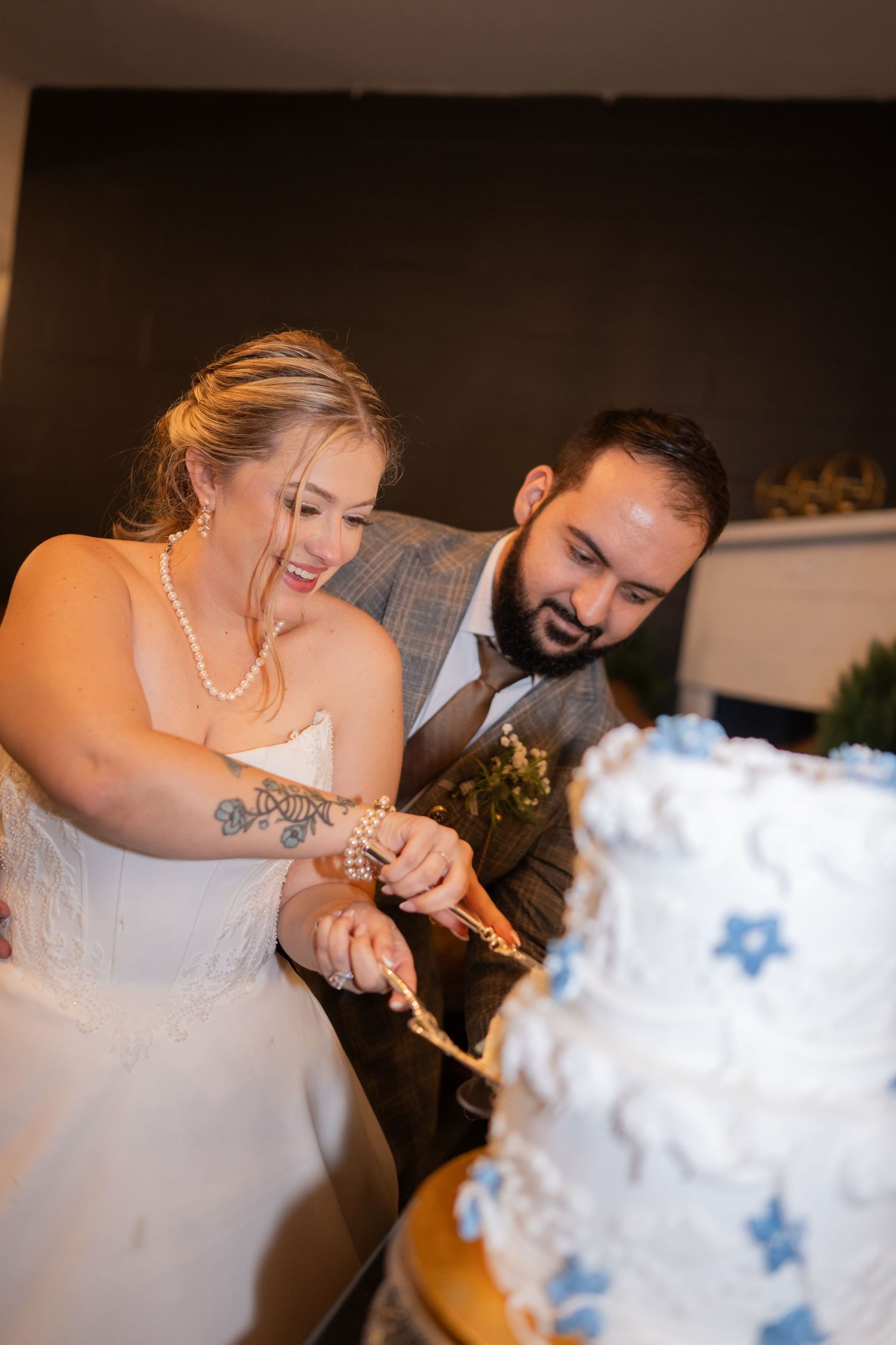 A couple cuts into their white wedding cake decorated with blue stars at their reception celebration.