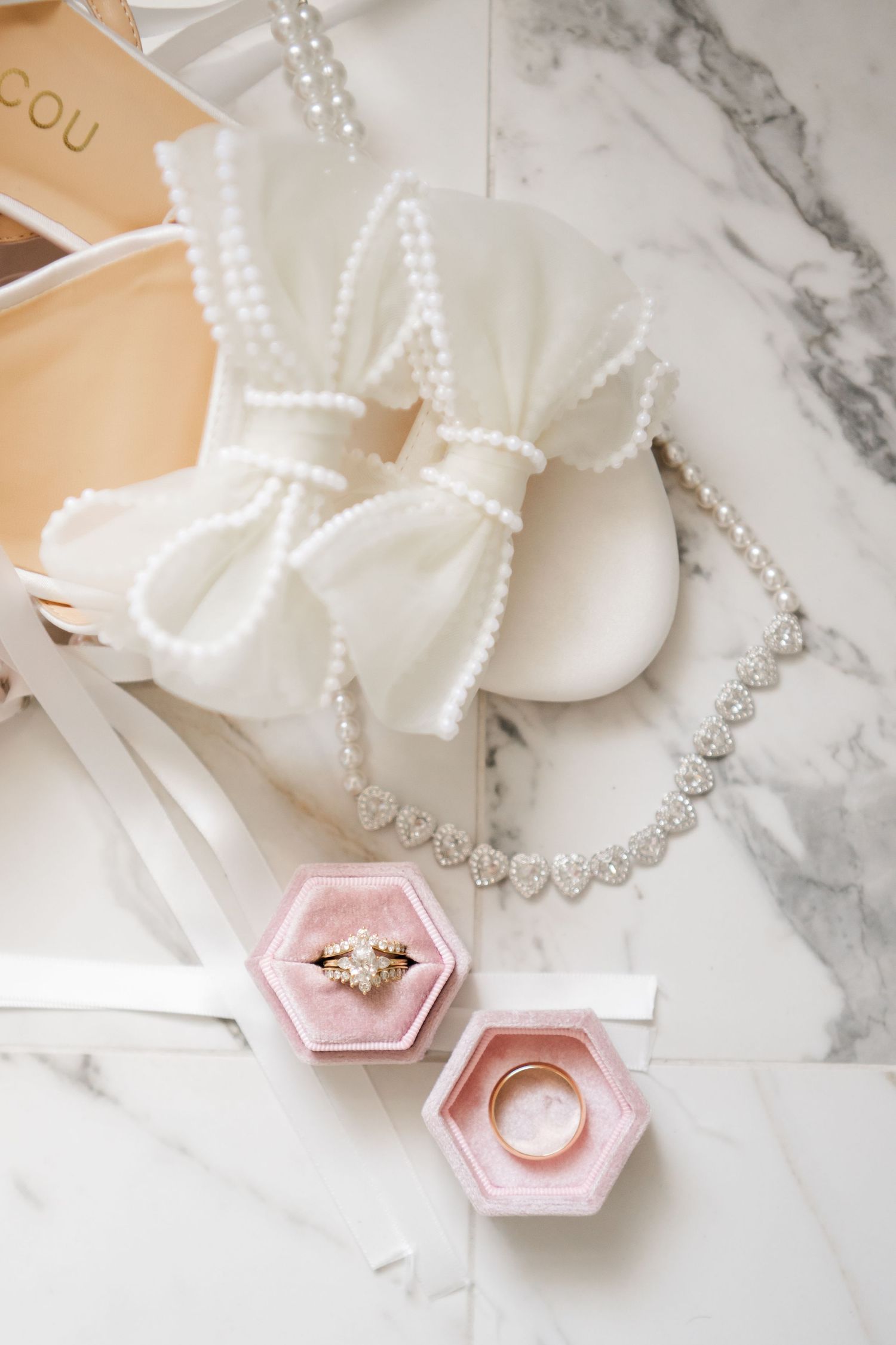 Wedding accessories including pearl necklace and pink hexagonal ring boxes on marble surface.