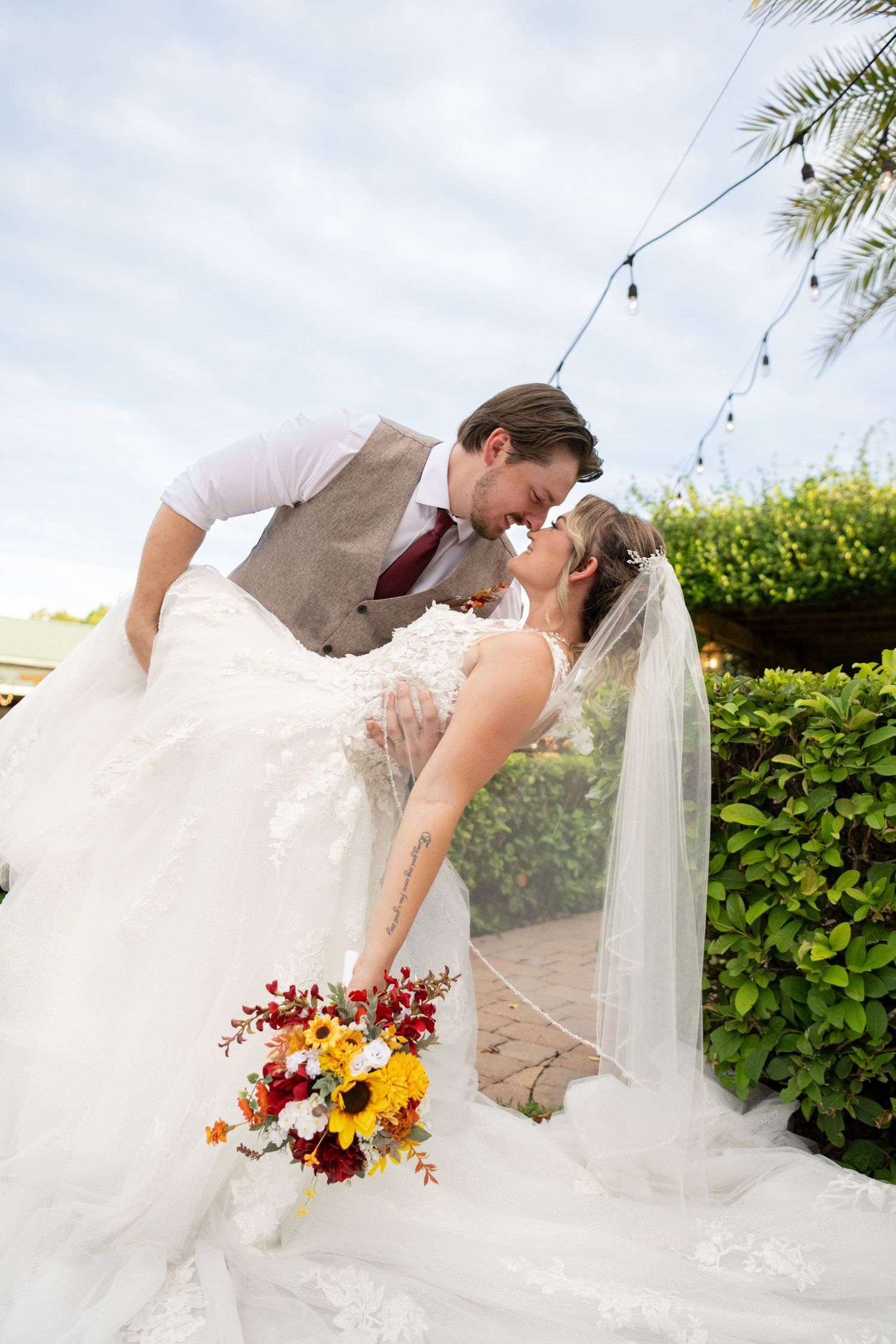 Romantic wedding couple sharing a kiss while bride's white dress and veil flow in the breeze with autumn flowers nearby.