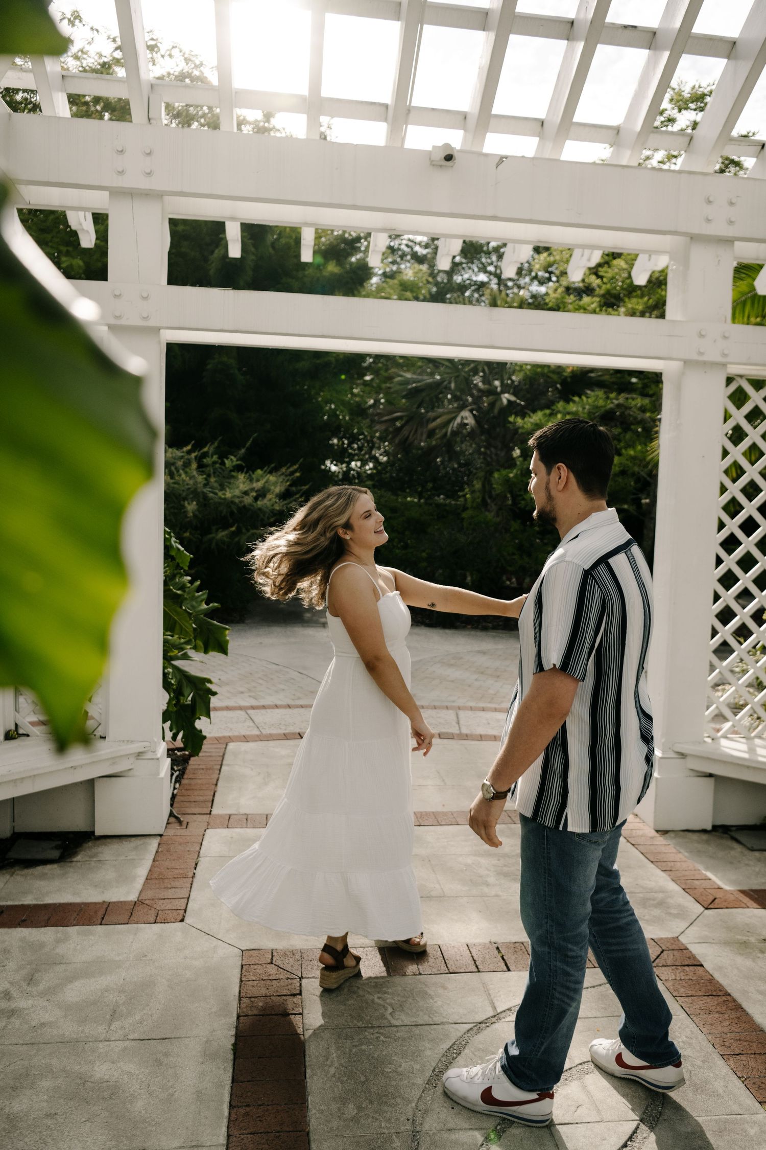 A couple dancing under a white pergola in a garden setting.