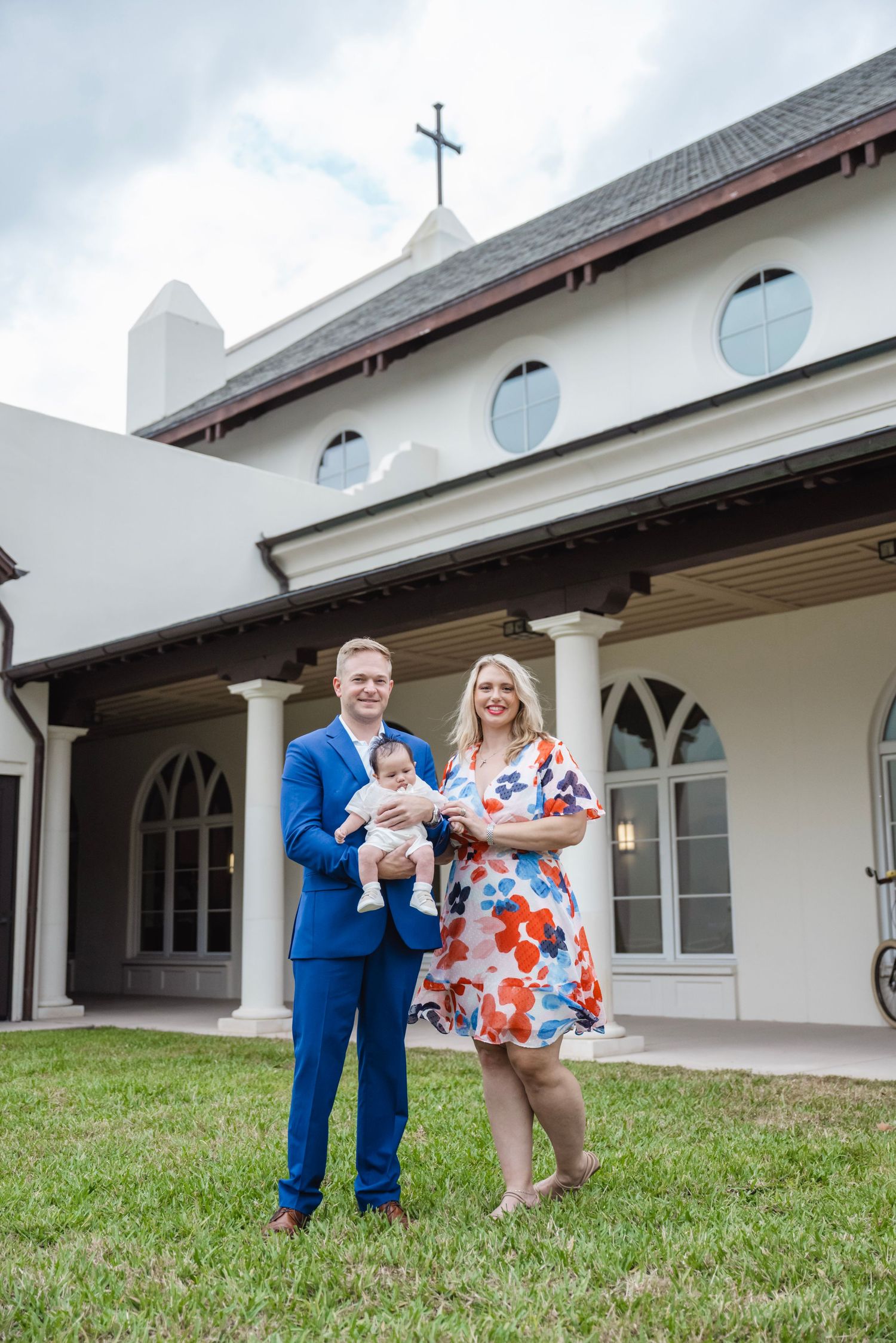 Family poses outside white church building with cross and arched windows.