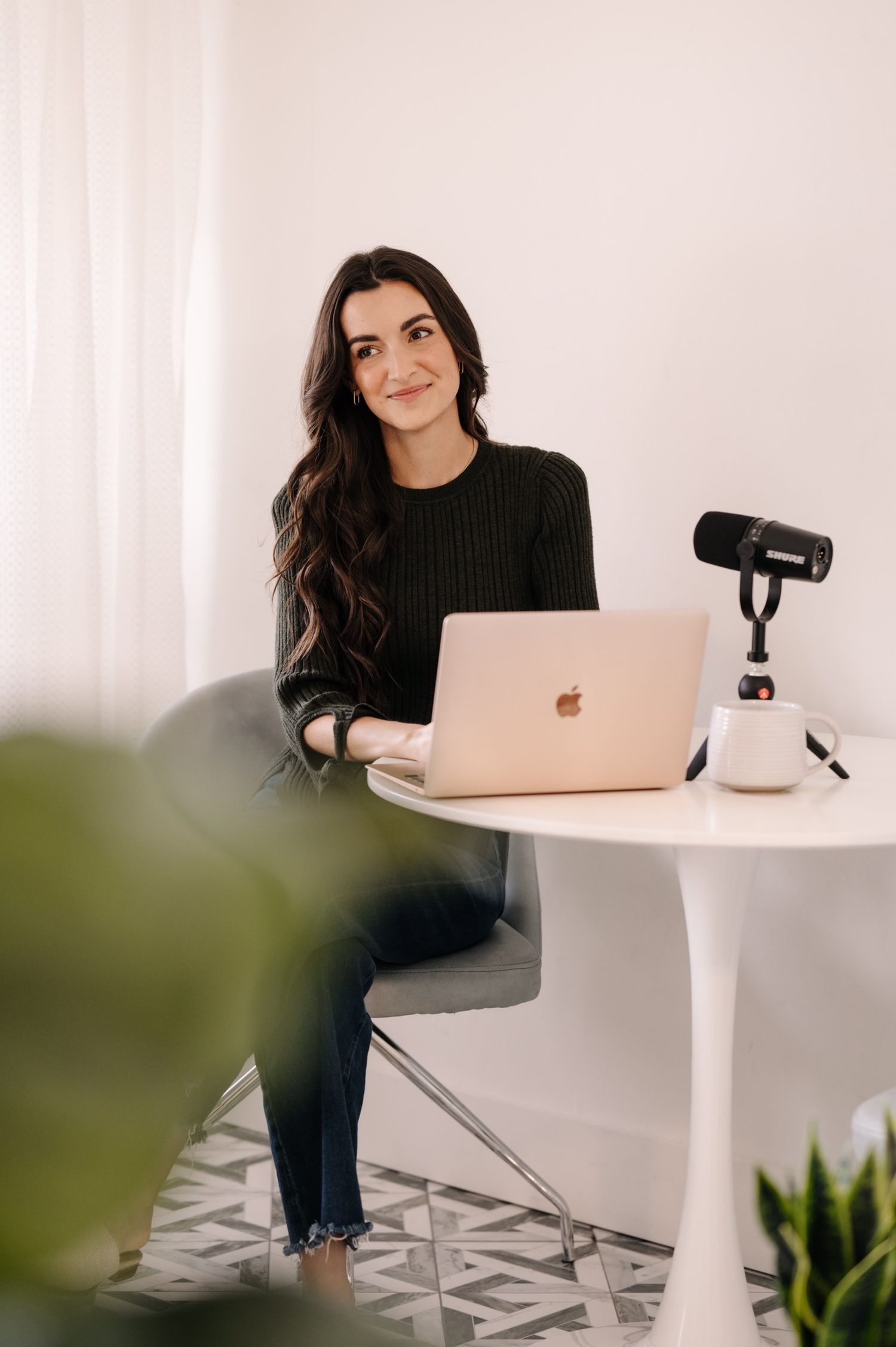 Modern workspace setup with person at white desk using laptop and microphone.