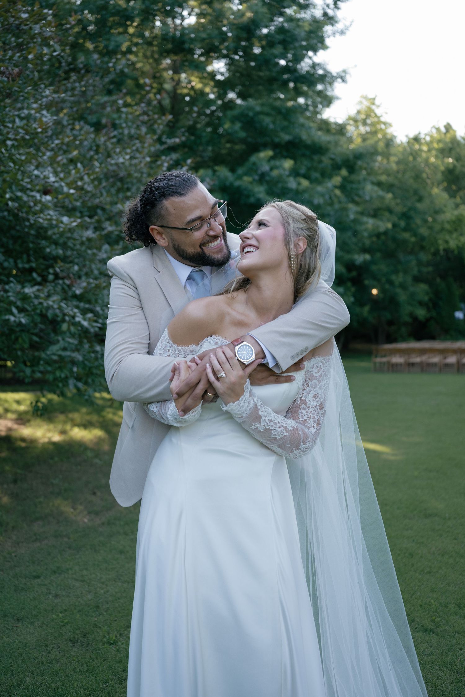 Bride and groom embrace and laugh together outdoors in a lush green garden during their wedding day.