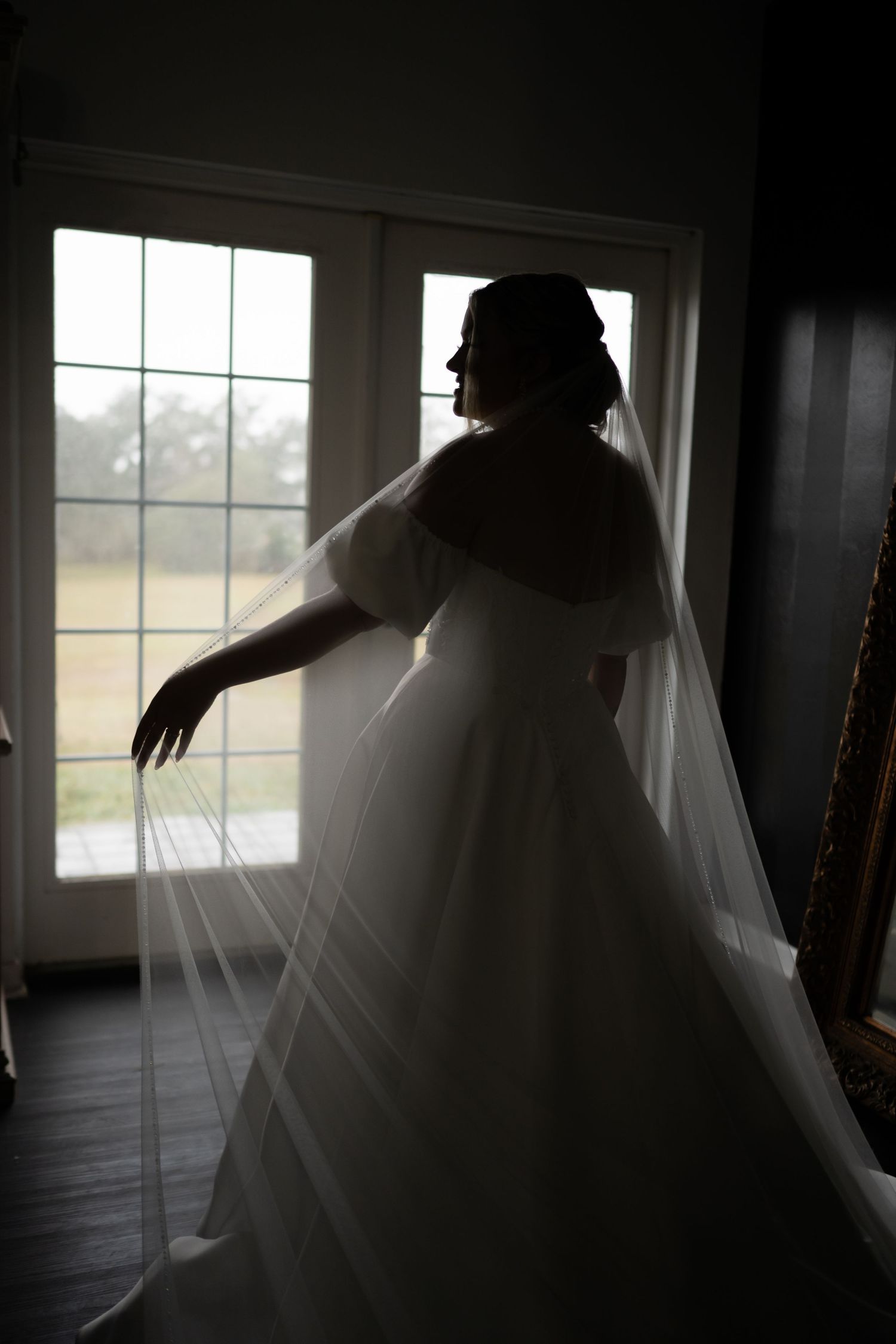 Ethereal silhouette of flowing wedding dress against bright window light.