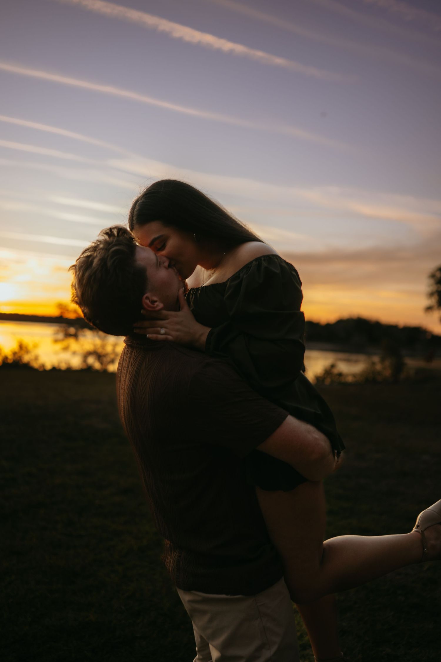 A romantic silhouette of a couple embracing against a golden sunset sky over a serene landscape.