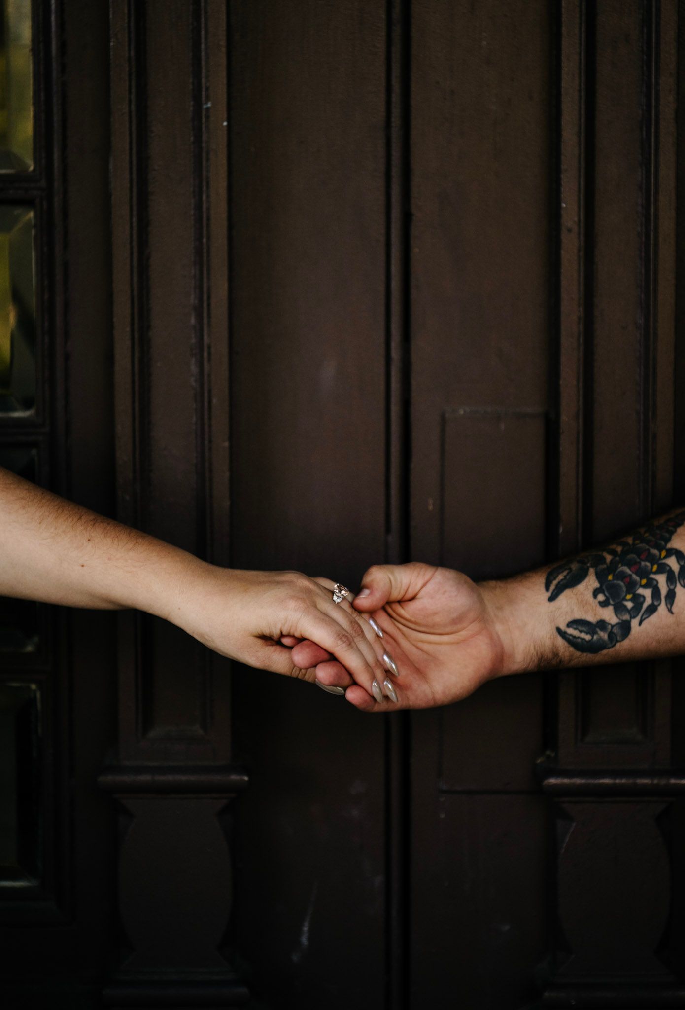 Two hands tenderly touch against a dark wooden door background.