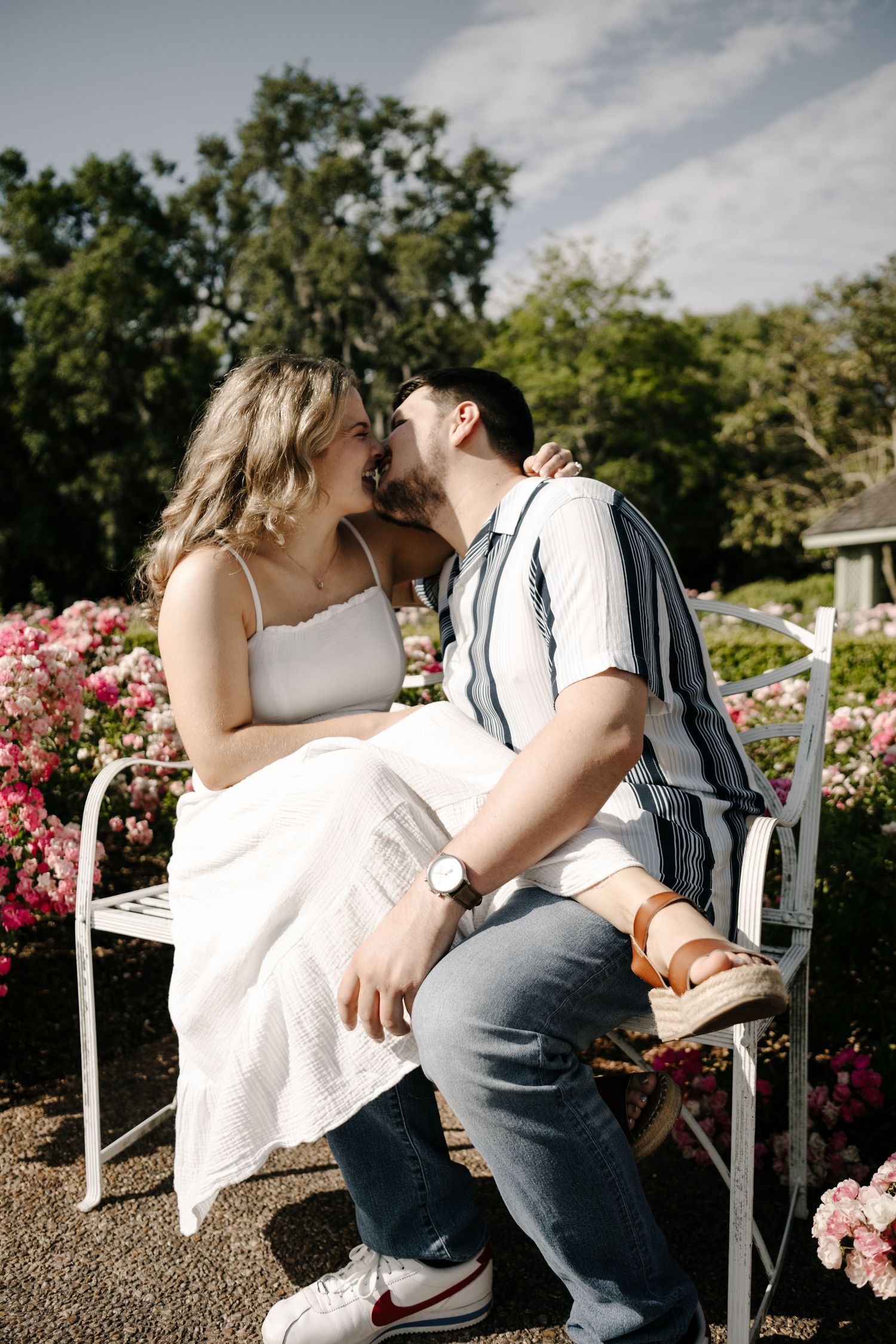 A couple sharing an intimate moment on a white bench surrounded by pink roses.