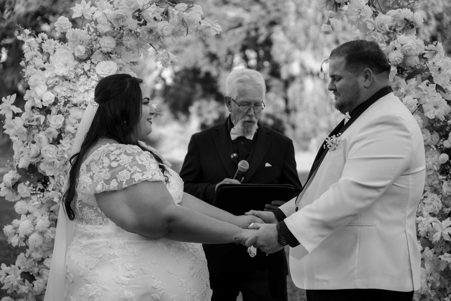 Black and white wedding ceremony moment captured with floral decorations in the background.