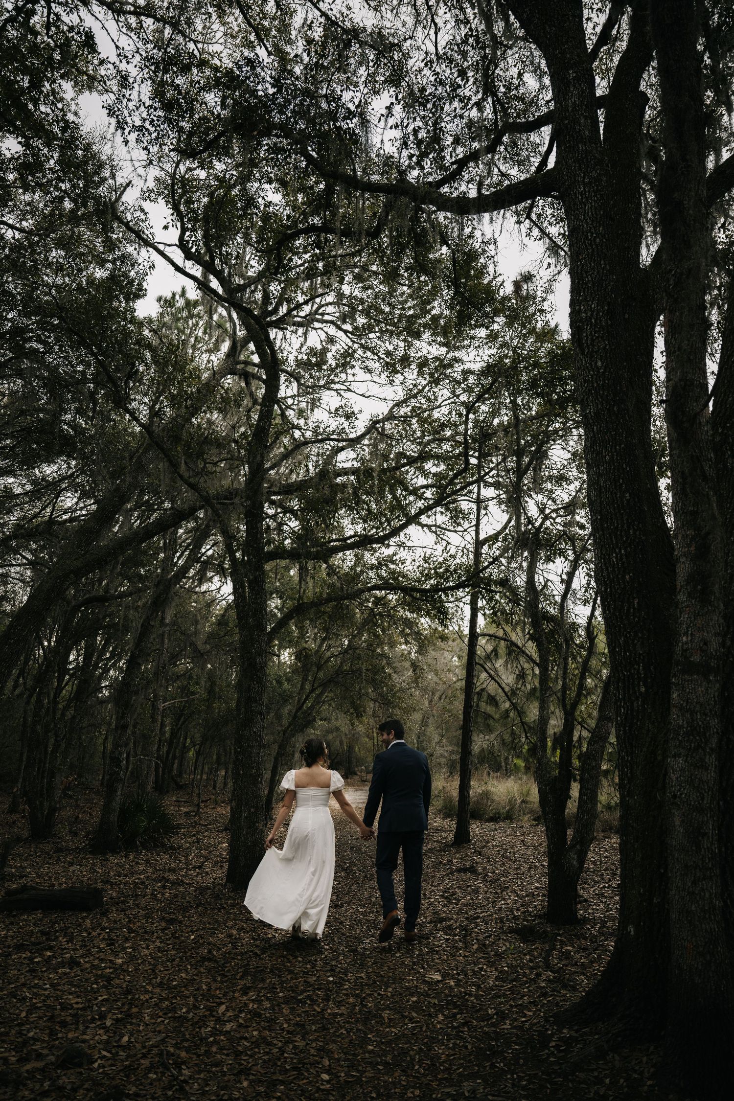 Newlyweds walk through a moody forest setting with fallen leaves.