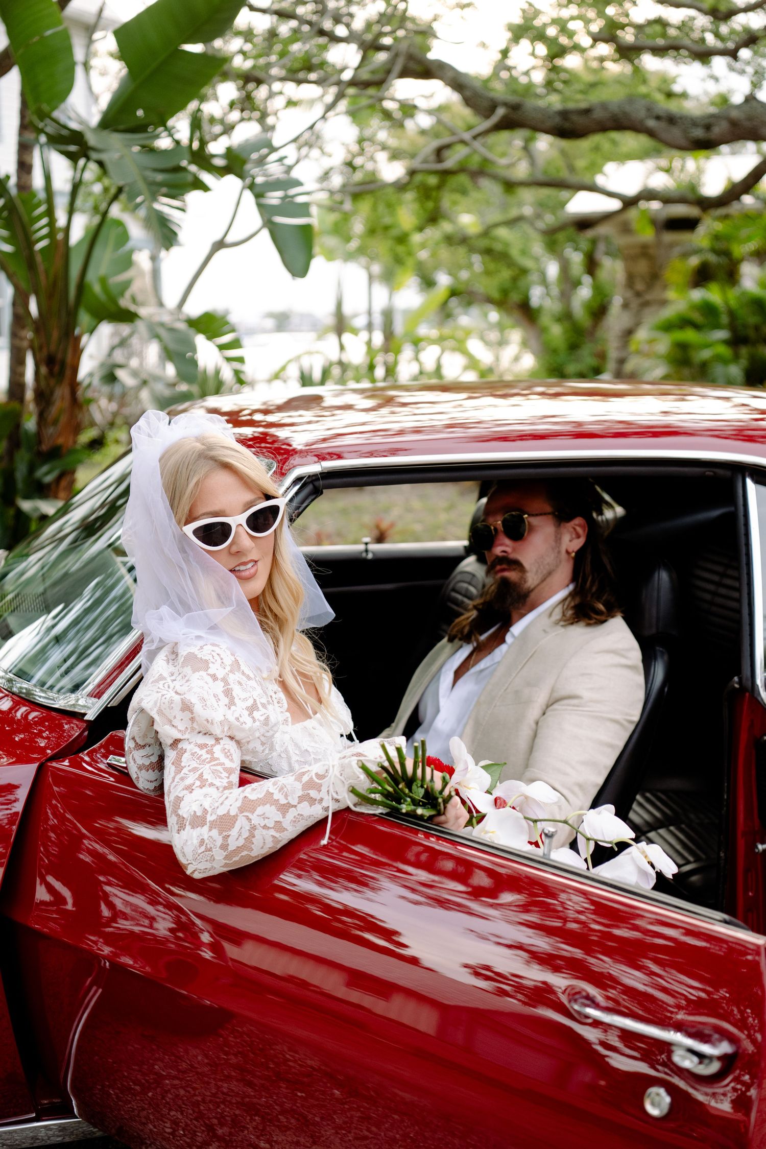 Wedding party riding in classic red car wearing vintage sunglasses.