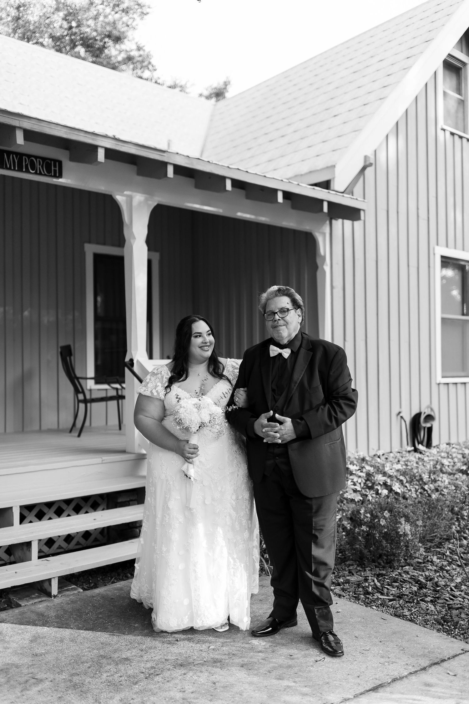 Wedding party members standing on a white porch of a rustic building.