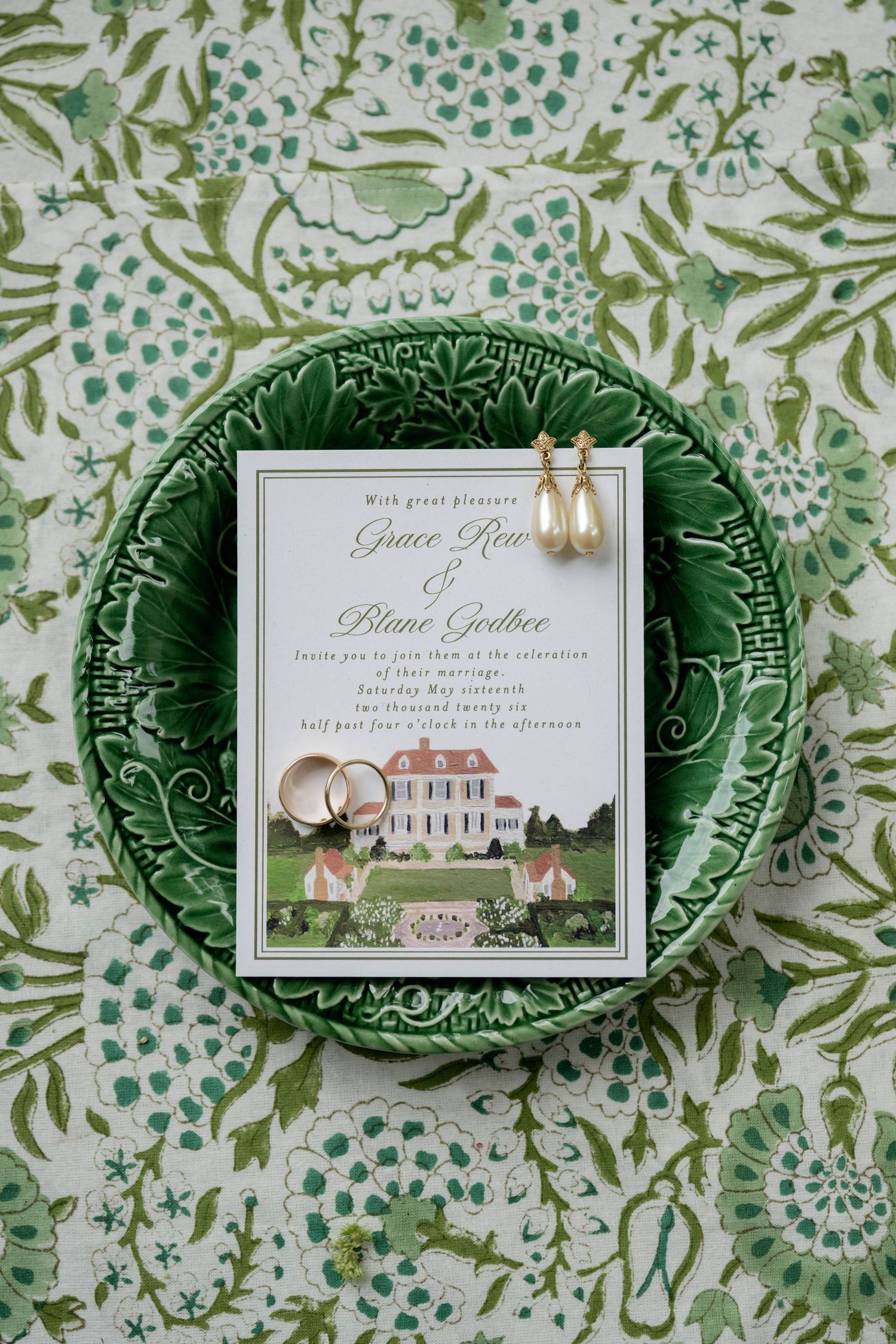 Wedding invitation for Grace Row and Blane Godbee on green cabbage leaf plate with gold pearl earrings and rings.
