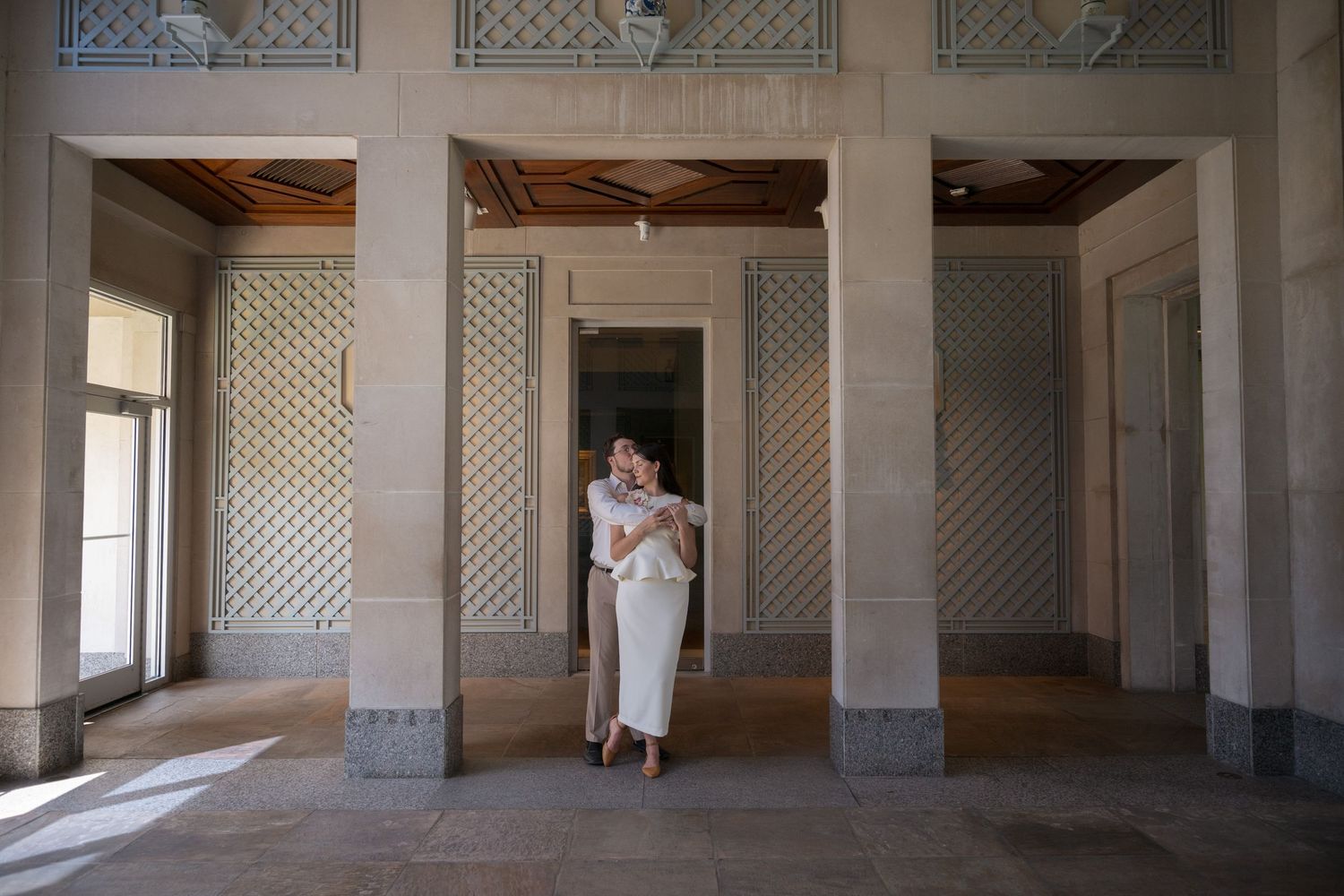 Couple embracing in an elegant architectural space with ornate lattice walls and marble columns.