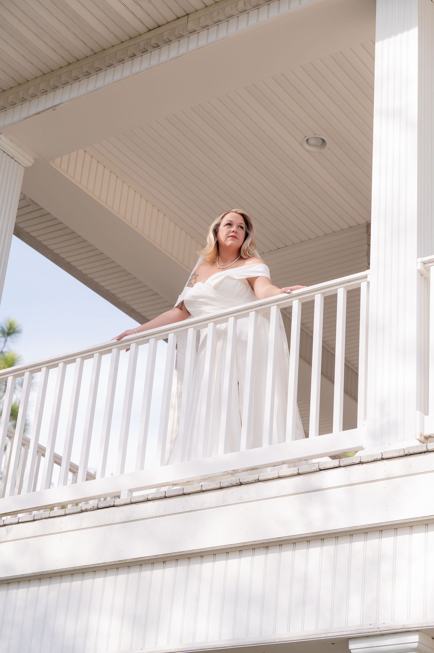 Bright outdoor balcony with white railings and beadboard ceiling overlooking sunny landscape.