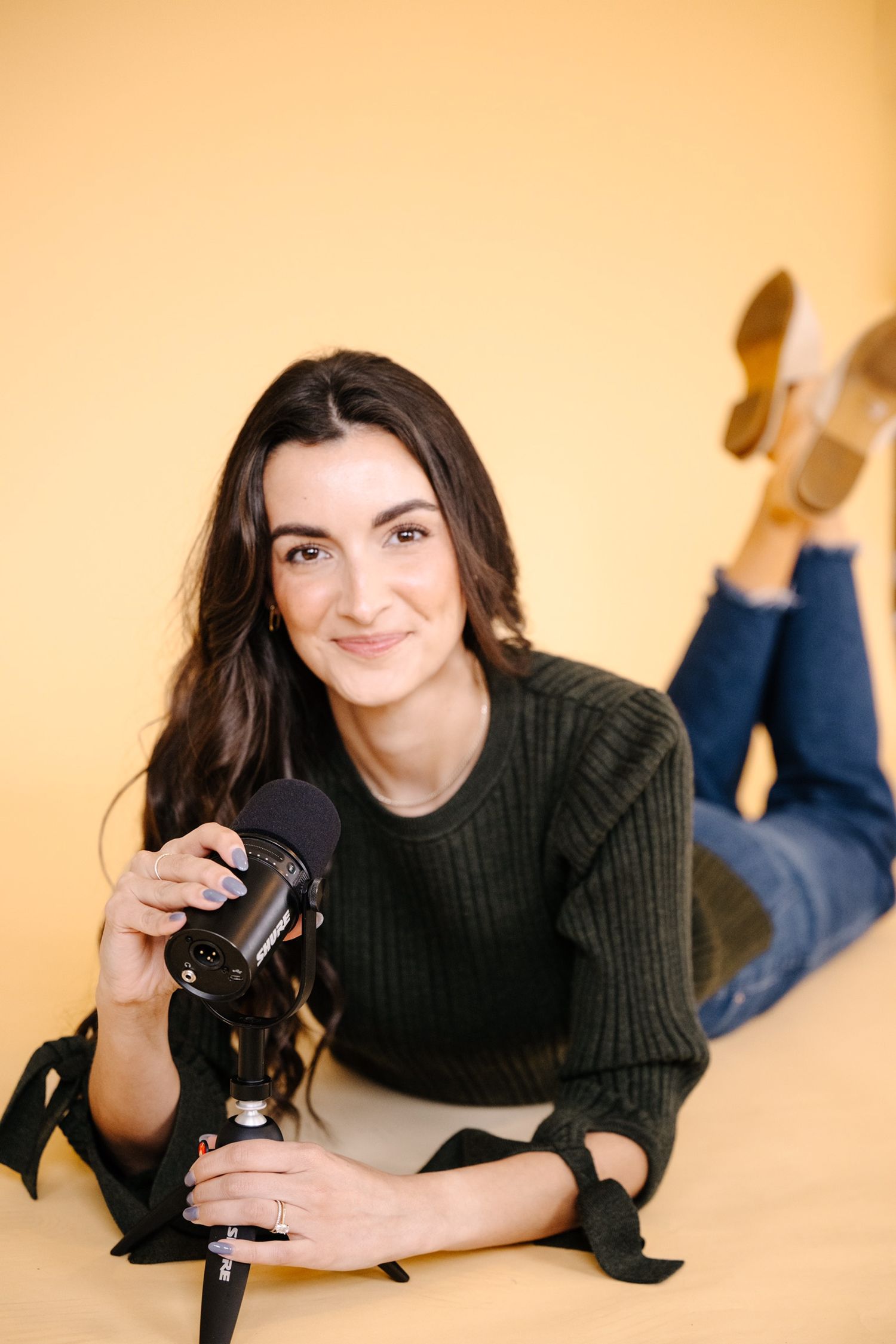 Person in black sweater poses with camera on warm orange background.