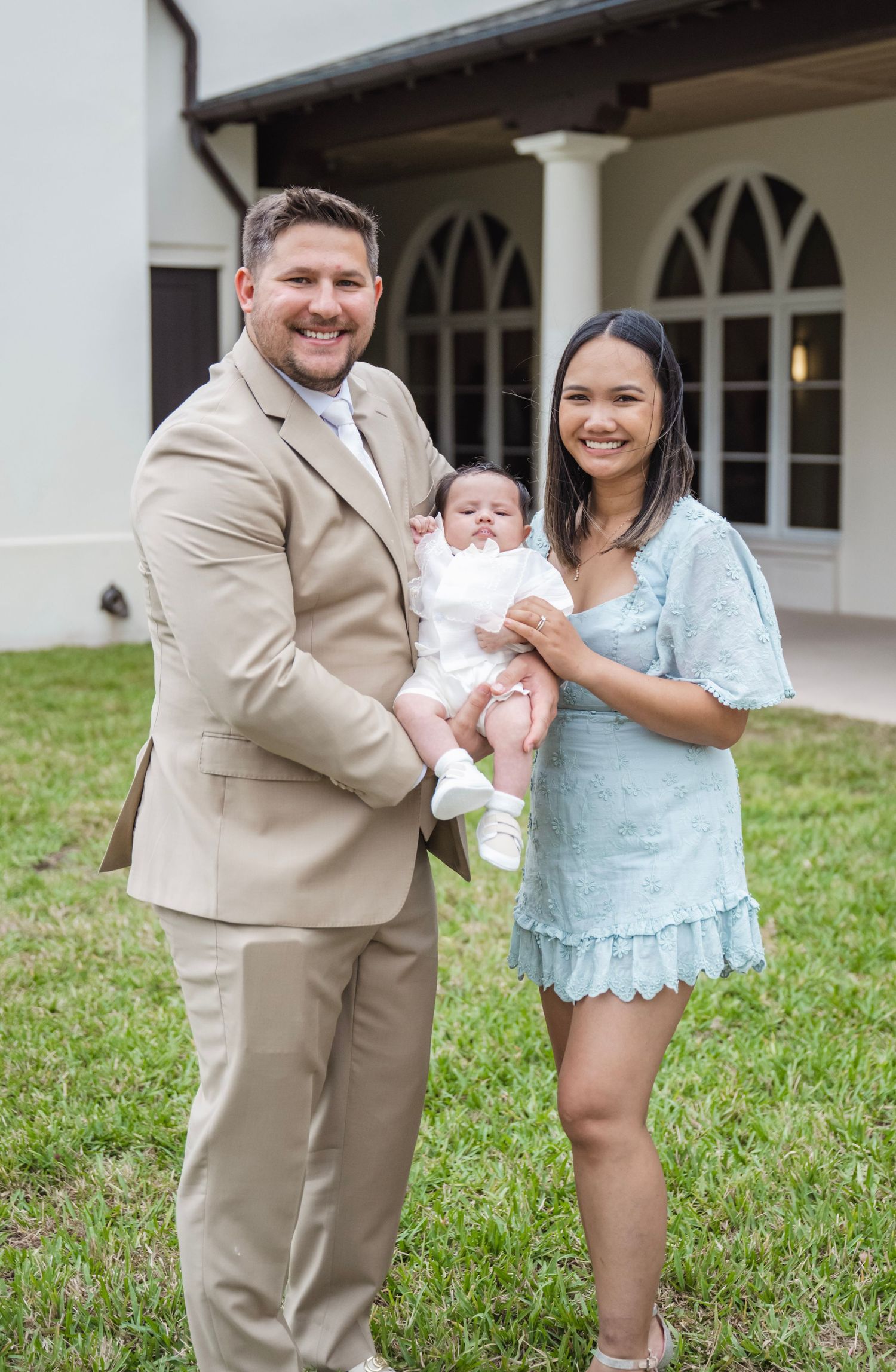 Family poses together on church grounds wearing coordinating beige and blue outfits.