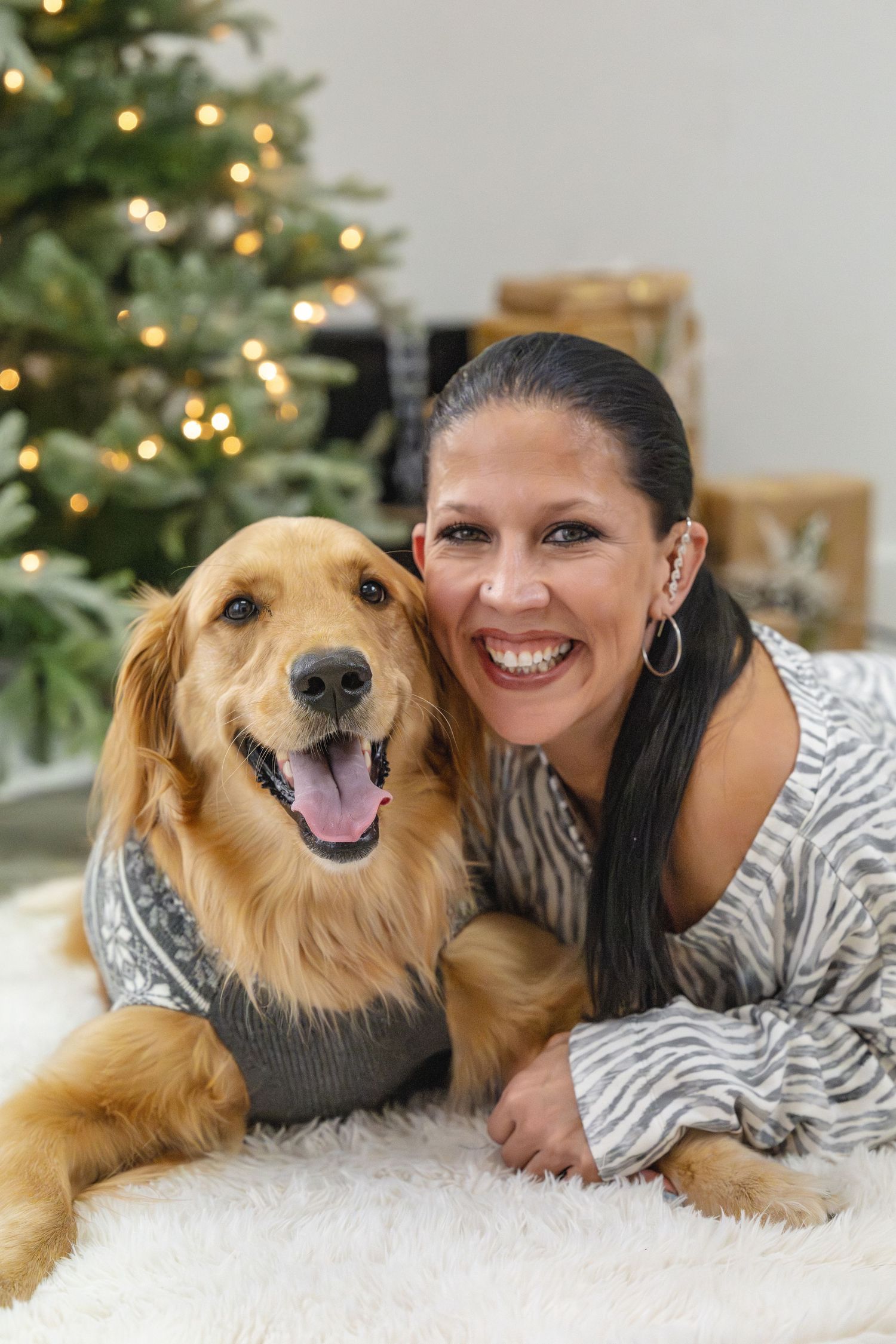 Golden retriever and person posing on white rug with Christmas tree in background.