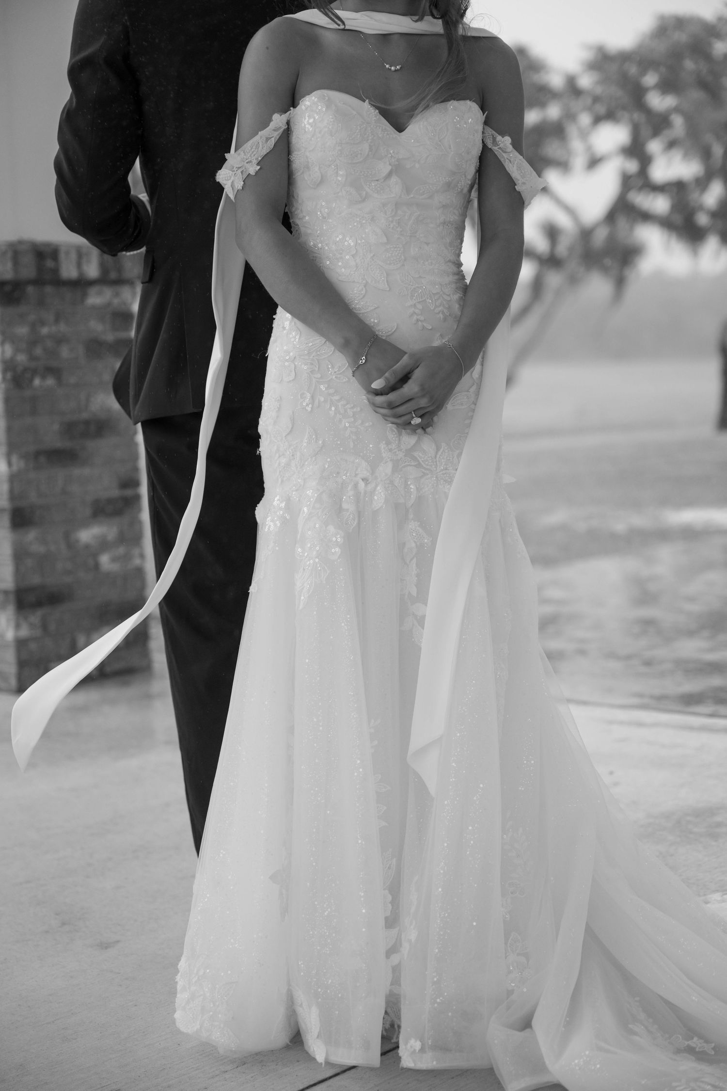 Black and white photo of a bride in a lace sweetheart gown standing beside a groom in a suit.