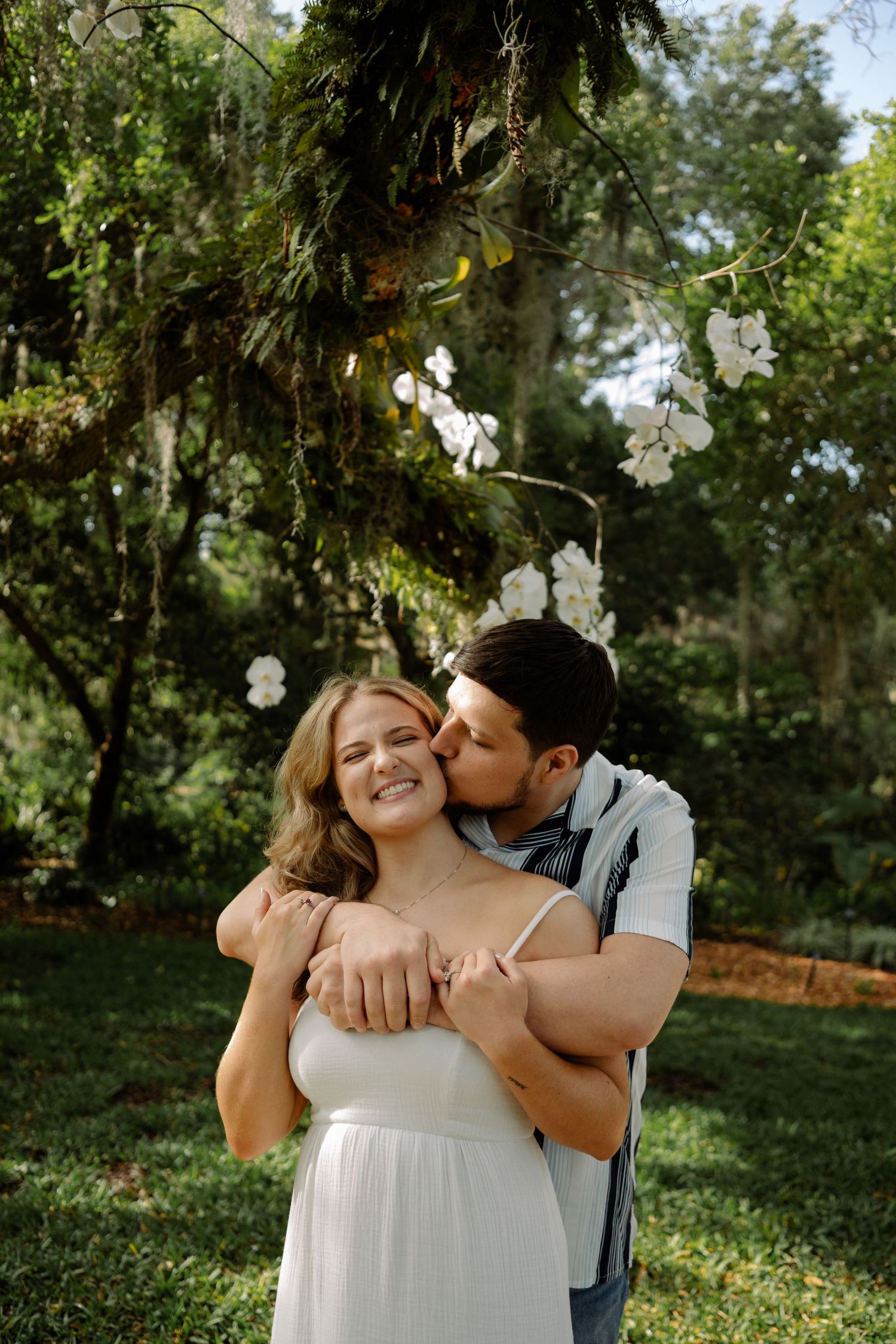 Romantic outdoor photoshoot in a lush green garden with hanging white floral decorations.