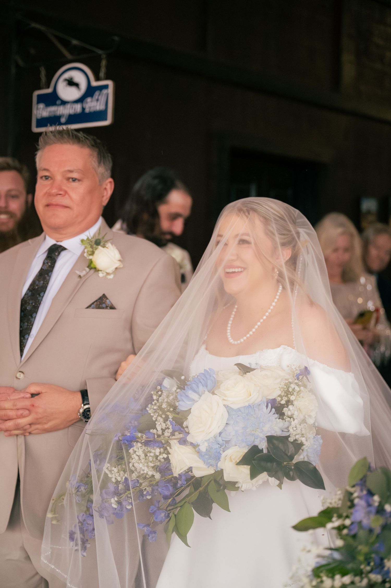 Wedding ceremony with bride in white dress and groom in tan suit holding blue and white floral bouquets.
