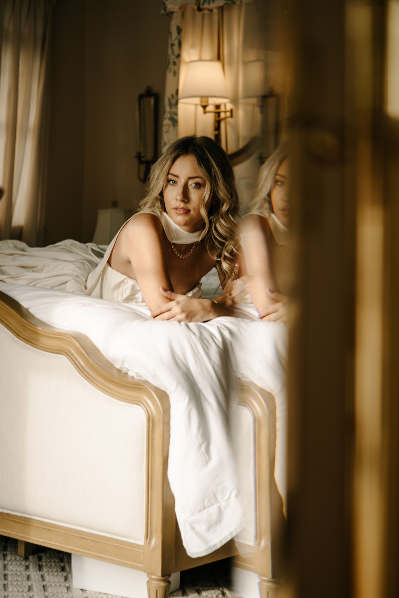 Elegant boudoir scene with soft lighting and white bedding in vintage-style bedroom.