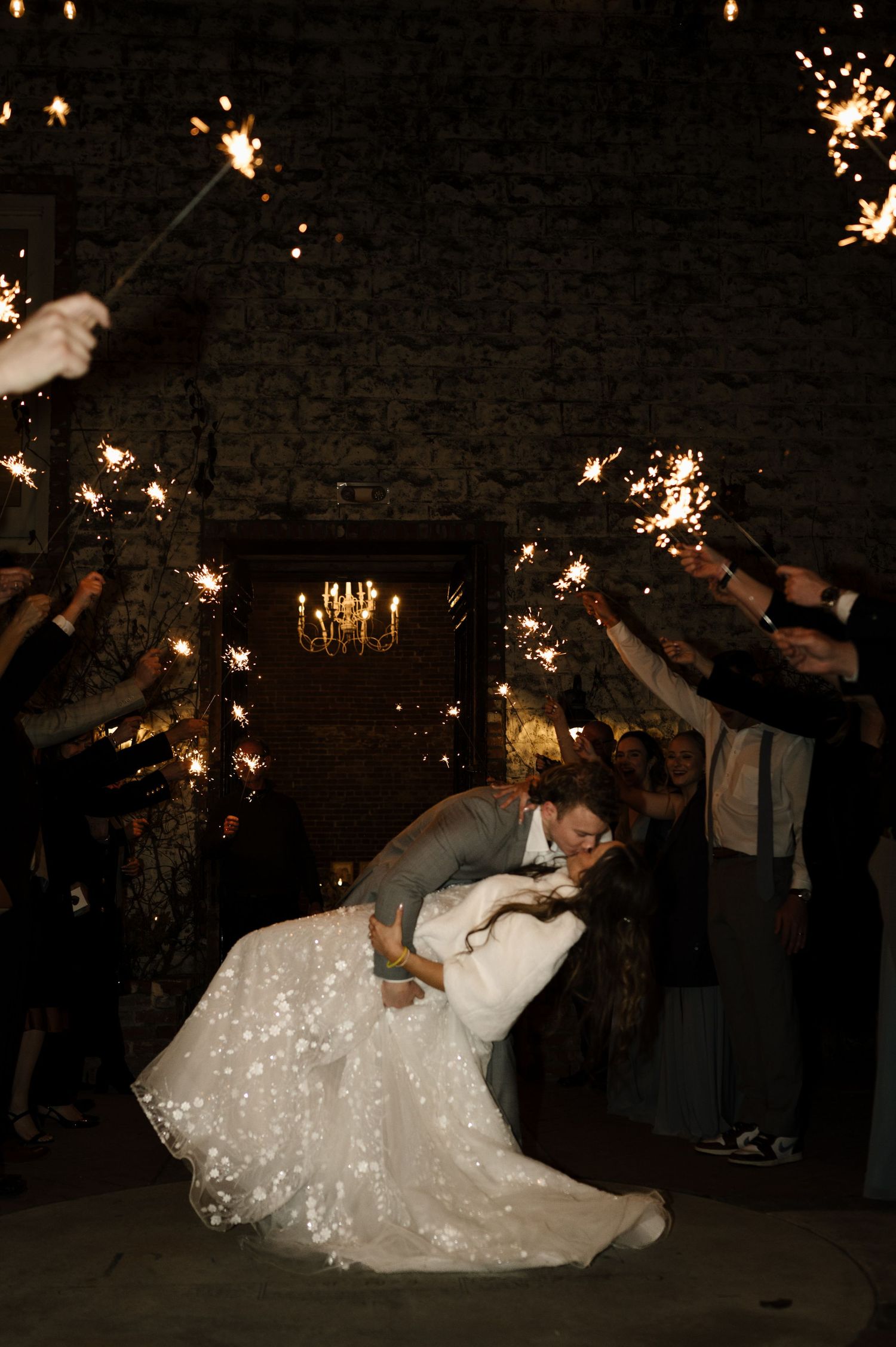 Bride and groom share a romantic dip kiss during a sparkler send-off at their wedding reception.