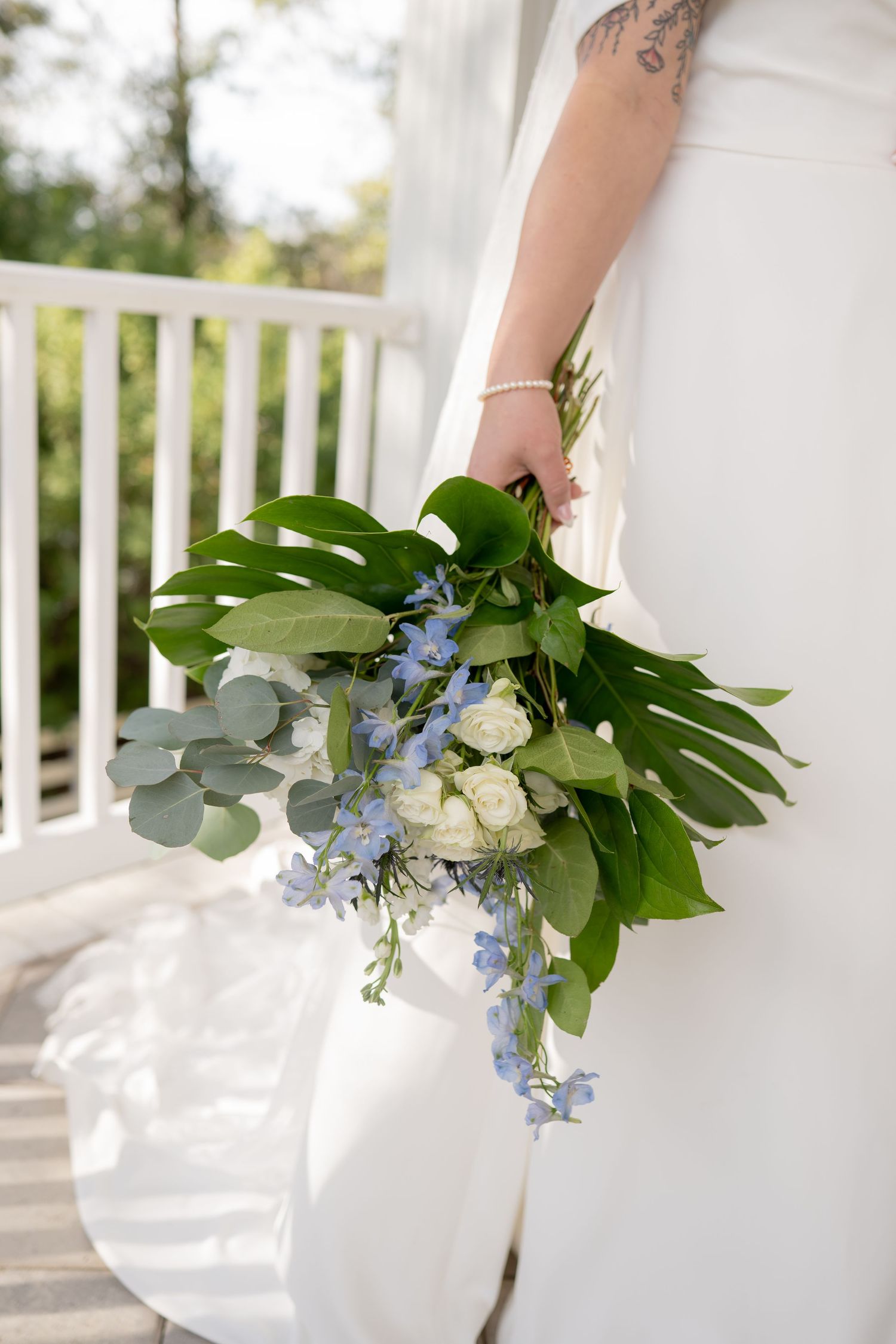 White and blue floral wedding bouquet with eucalyptus leaves against white railing.