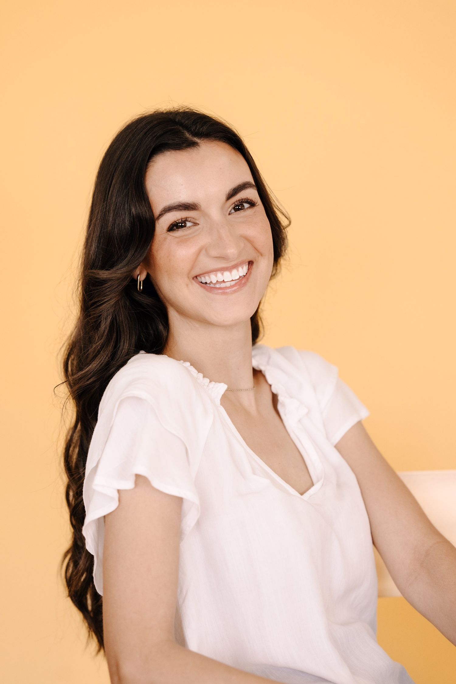 Portrait series with person in white ruffled blouse against warm orange background.