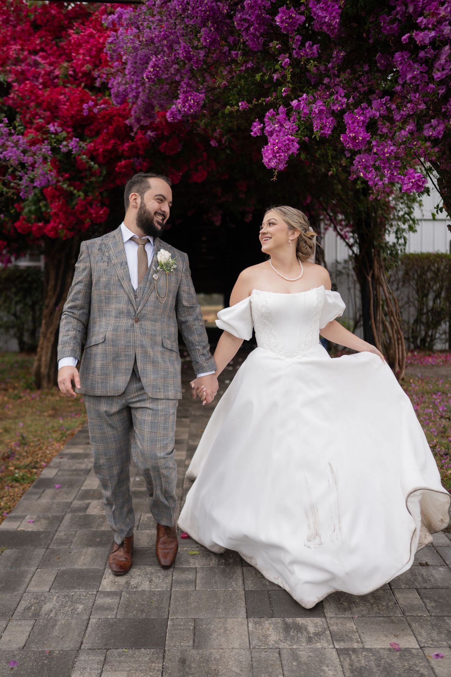 Newlyweds walking together against vibrant purple and red flowering trees.