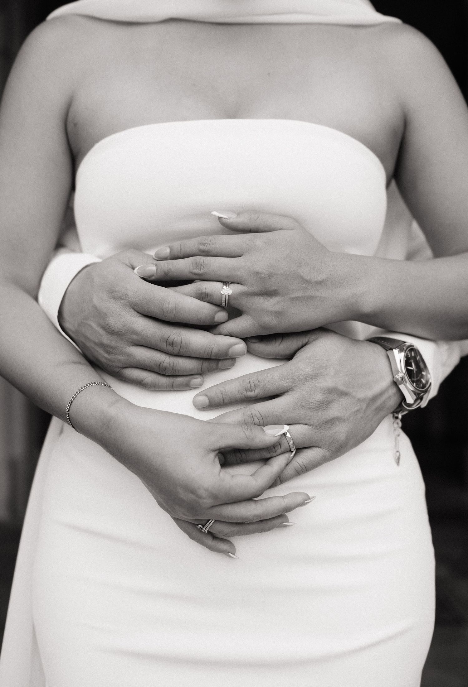 Black and white photo of newlyweds hands with wedding rings resting on brides white gown.