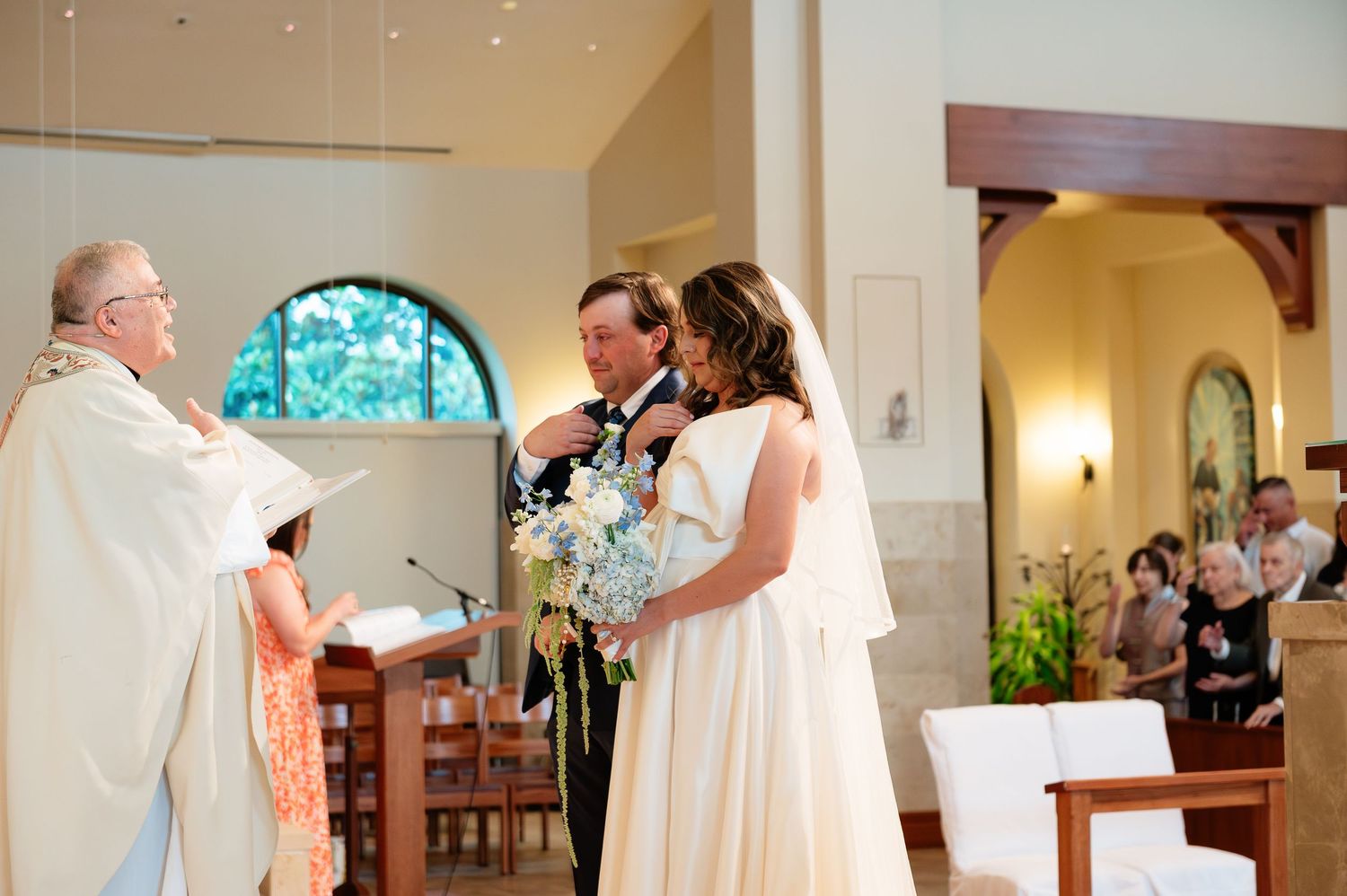 Bride and groom exchanging vows at church altar with officiant during elegant wedding ceremony.
